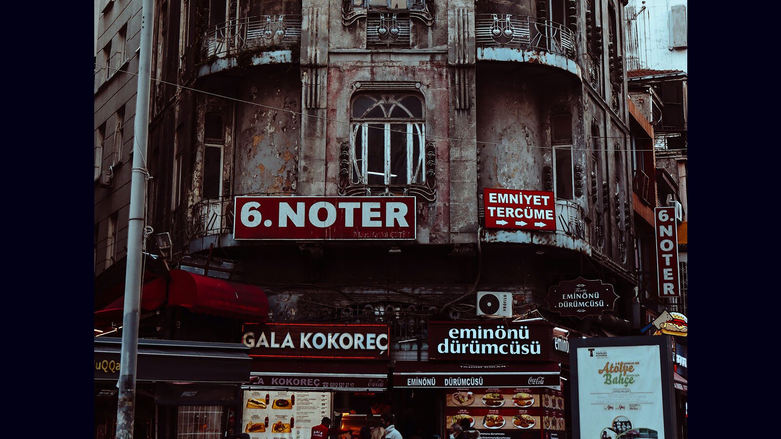 Zdjęcie przedstawia front starej kamienicy, na którym umieszczono dużo szyldów. 