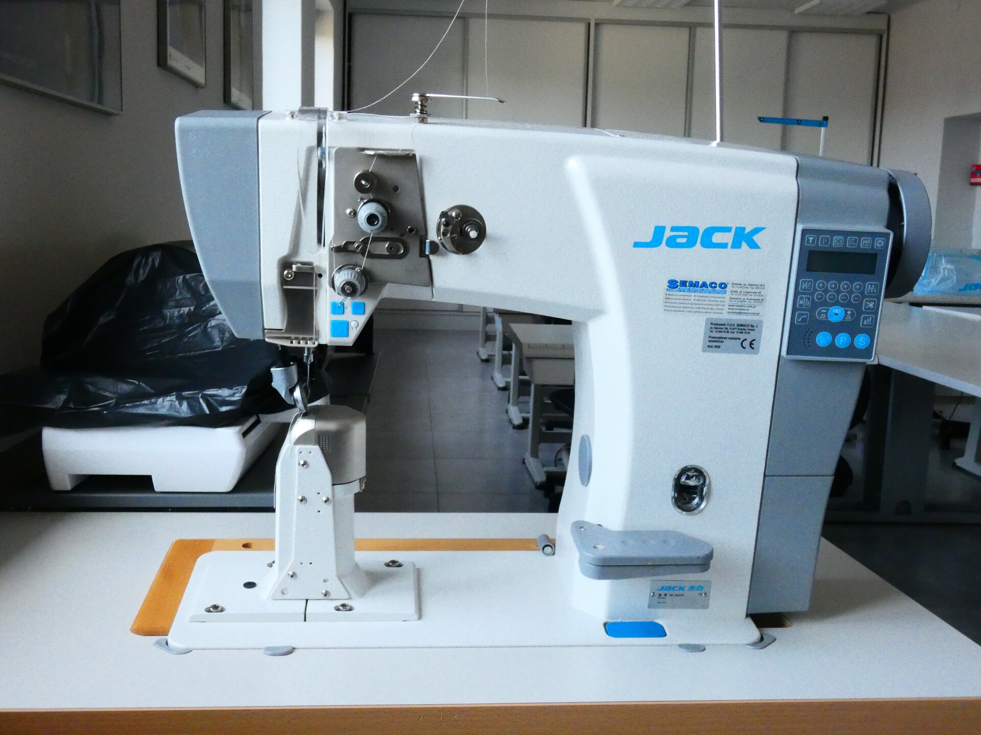 Zdjęcie przedstawia białą maszynę z szarymi oraz niebieskimi elementami. Po prawej stronie znajduje się szary panel sterujący.