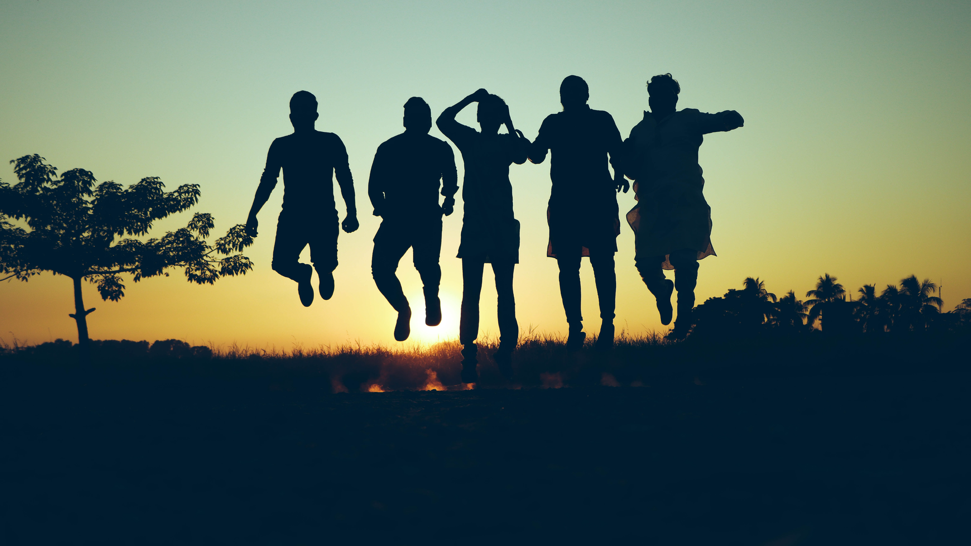 Zdjęcie przedstawia ujęcie pod słońce. Na zdjęciu znajdują się sylwetki pięciu osób. Ujęcie zostało wykonane w momencie gdy wszystkie osoby podskoczyły. Osoby na zdjęciu nie dotykają ziemi.