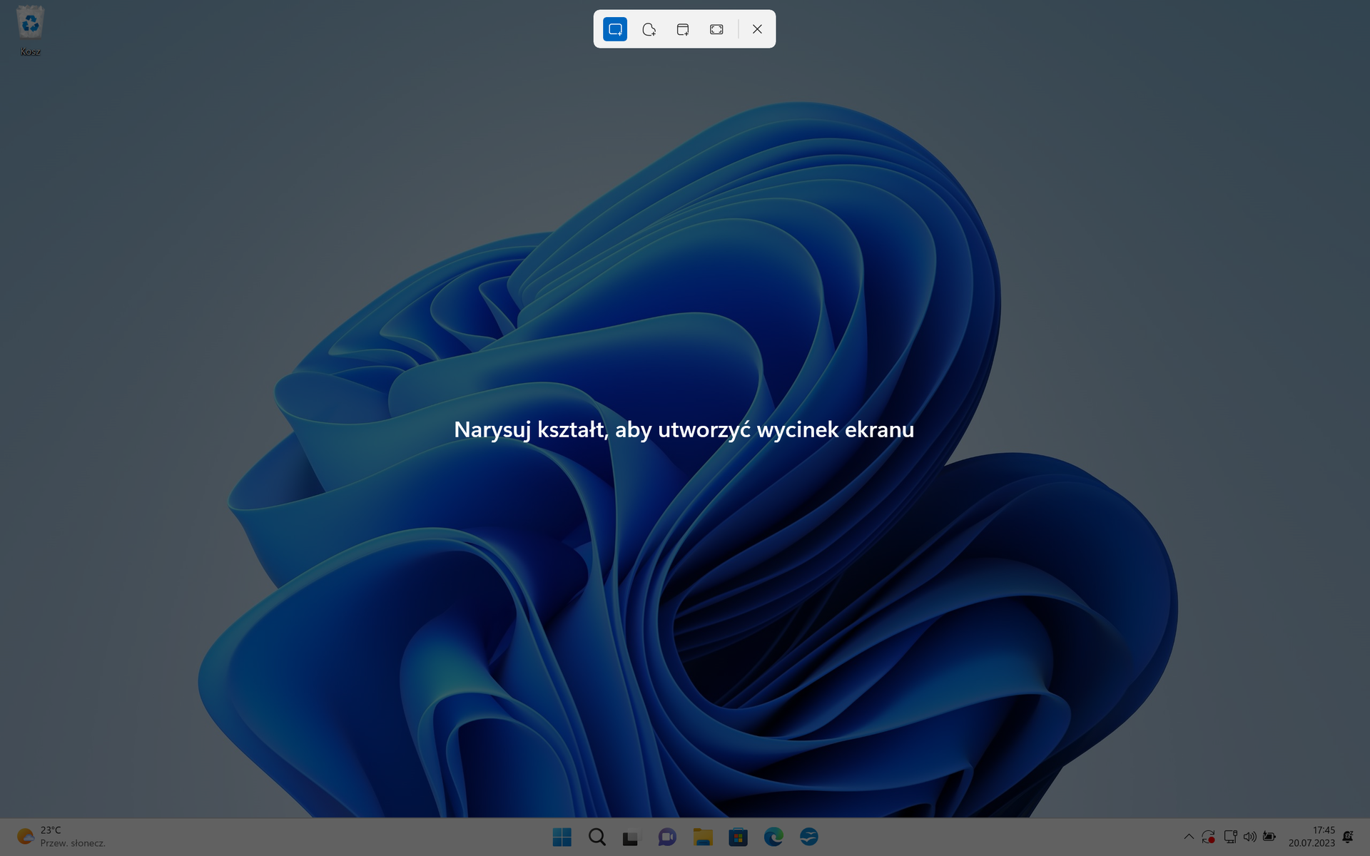 Ilustracja przedstawia przyciemniony pulpit systemu Windows 11. Na tapecie znajduje się niebieskie logo Windows. Na samym środku znajduje się napis Narysuj kształt, aby stworzyć wycinek ekranu.