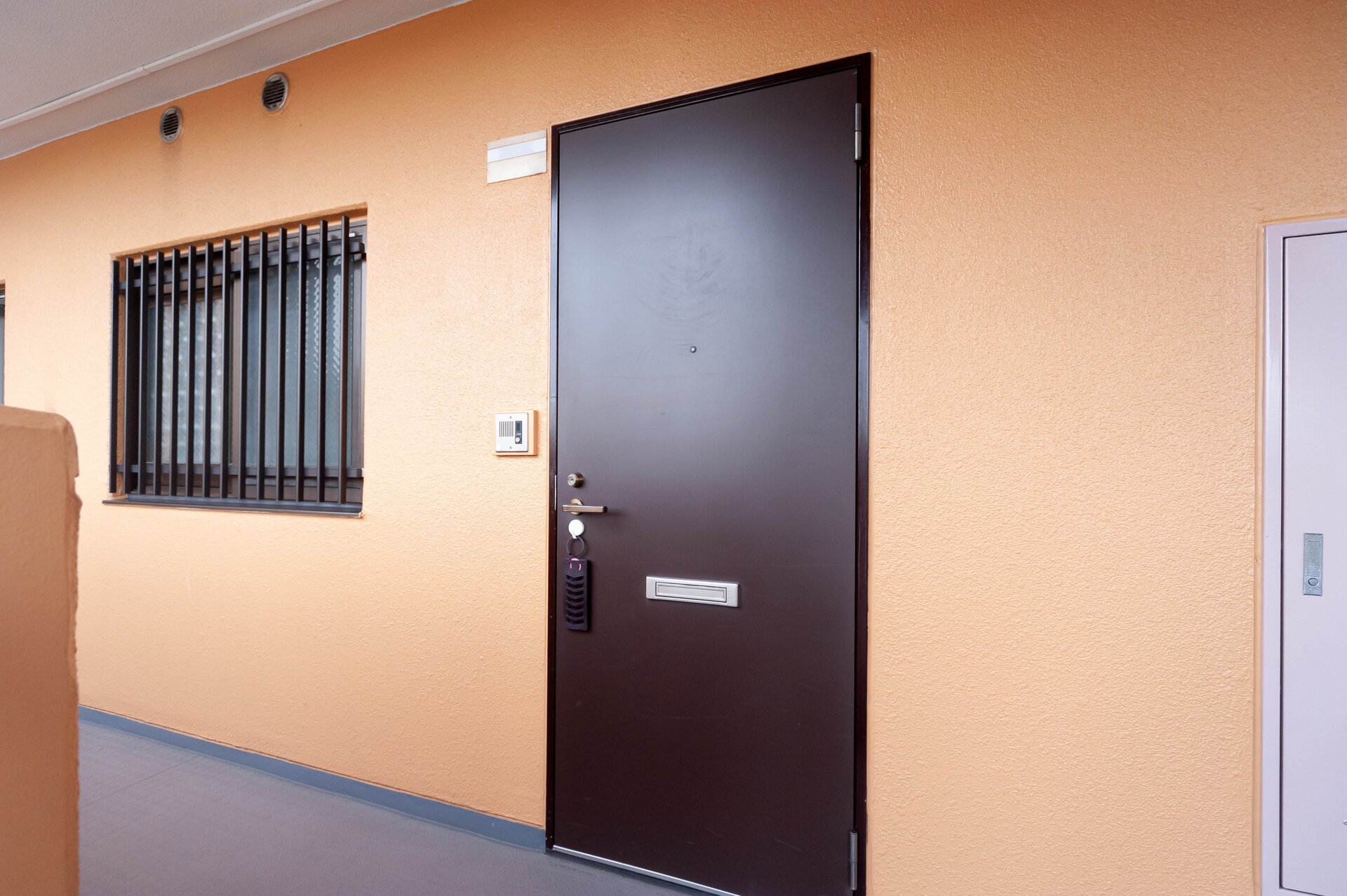 Zdjęcie przedstawia ciemnobrązowe drzwi aluminiowe, do których przymocowane jest urządzenie do wpisywania kodu otwierającego.