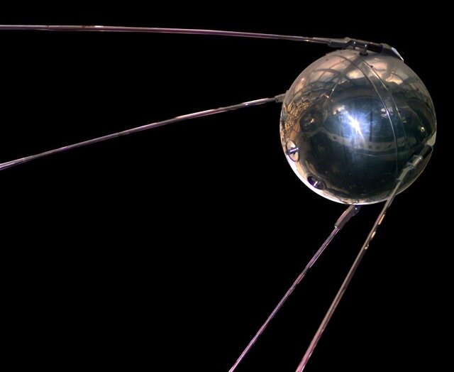 Na fotografii znajduje się sztuczny satelita Sputnik. Ma on formę metalowej kuli, do której pod kątem 35° przymocowane są cztery anteny.  Sputnik znajduje się na czarnym tle.
