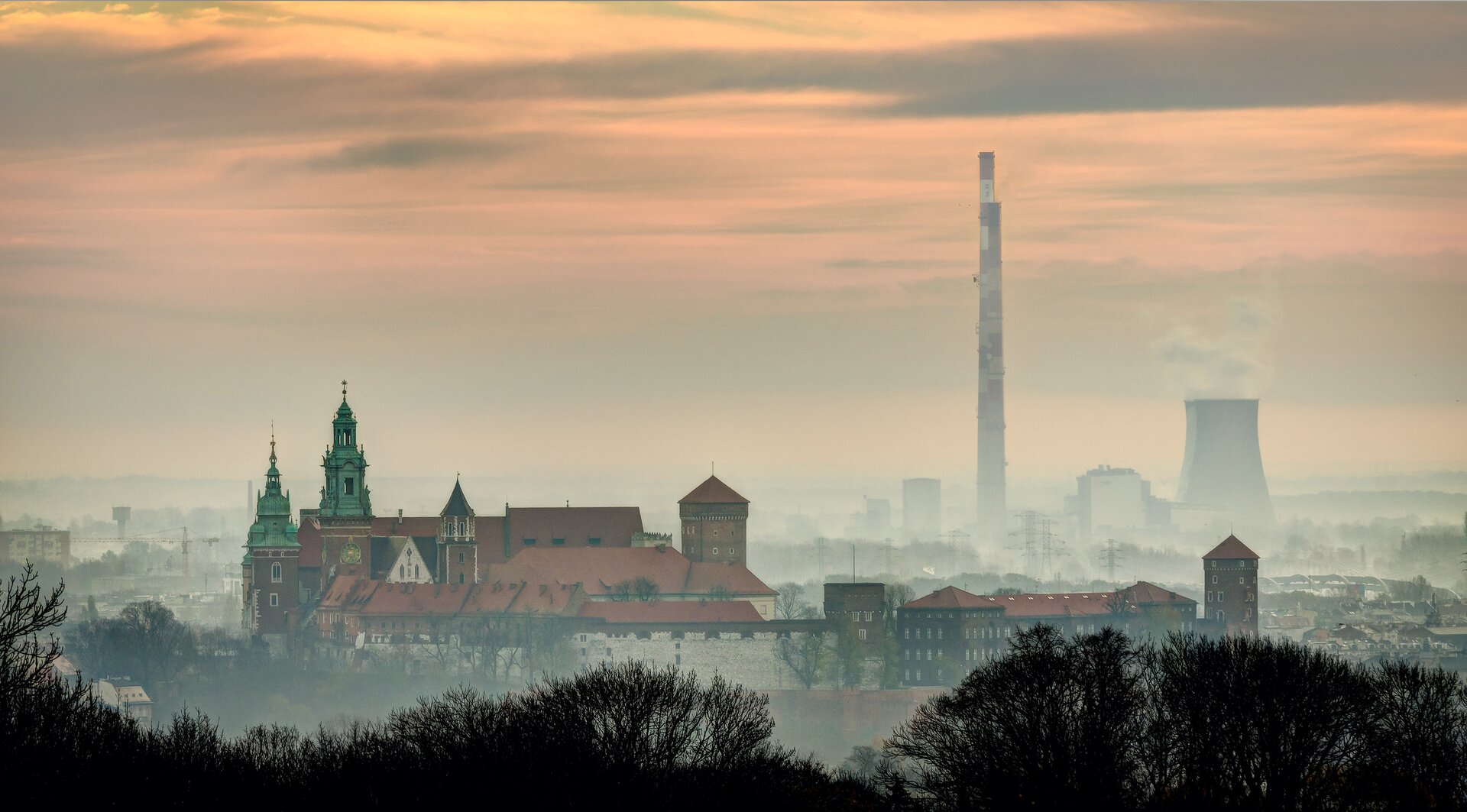 Zdjęcie przedstawia smog kwaśny. Za smogiem znajdują się historyczne zabudowania miasta. W tle jest komin fabryczny.