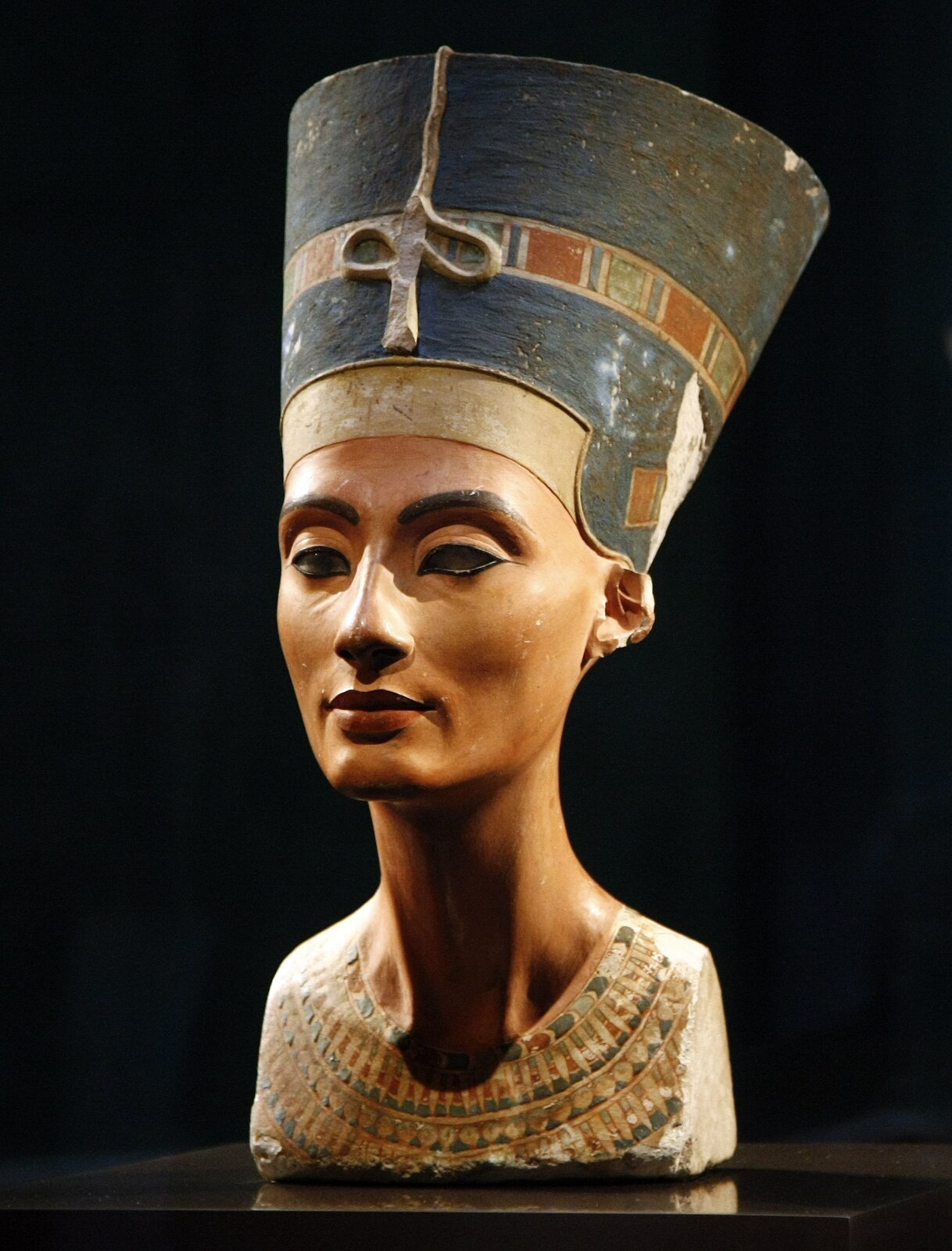 Ilustracja przedstawia pracę Totmesa pt. „Popiersie Nefertiti" (Nefretete). Obecnie znajduje się ono w Berlinie w Neues Museum-Muzeum Egipskie. Popiersie liczy 47 centymetrów i waży około 20 kilogramów. Zostało wyrzeźbione z wapienia i pokryte polichromowanym stiukiem. Jest to rzeźba pełnoplastyczna, zachowana w dobrym stanie mimo kilku ubytków (m.in. na wysokości ramion i górnej partii klatki piersiowej, na twarzy, uszach, a ponadto w tylnej partii nakrycia głowy). Głowa została nakryta wysmukłym czepcem oraz została osadzona na długiej szyi, na której widoczne są krtań i mięśnie. Nefertiti jest tu ukazana jako dorosła kobieta. Jej ciemno-niebieskie oczy są lekko przysłonięte powiekami, obwódki oczu są mocno podkreślone czarnym konturem. Lewe oko jest niepełne; brak tęczówki i źrenicy. Na jej ustach rysuje się lekki uśmiech. Ukazane zostały też w sposób subtelny policzki, zmarszczki i fałdy skórne (na powiekach, poniżej oczu oraz obok nosa). Na skroniach Nefertiti spoczywa wysoki ciemno-błękitny czepiec ozdobiony złotym diademem królewskim z charakterystycznymi prostokątnymi częściami w zielonkawych i rdzawych tonacjach. Z przodu diademu ureusz, w obecnym stanie silnie uszkodzony.