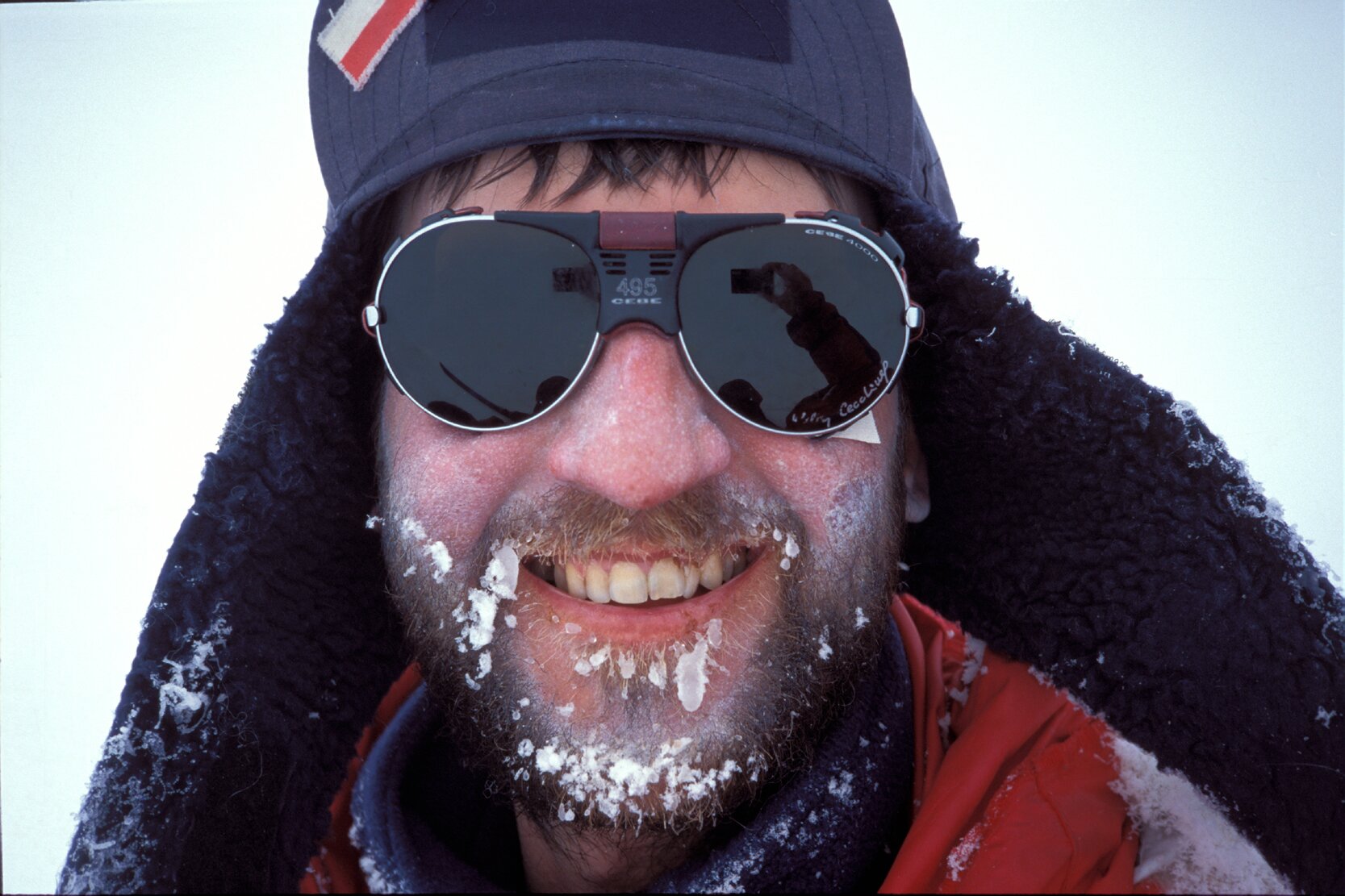 Marek Kamiński (Polak). Na zdjęciu uśmiechnięty mężczyzna w okularach przeciwsłonecznych i czapce uszance, robiący sobie zdjęcie. Na brodzie kawałki śniegu.