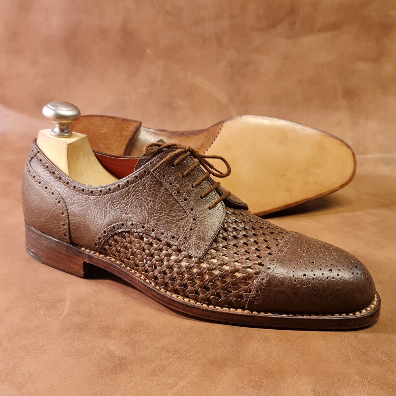 Zdjęcie przedstawia męski półbut w kolorze brązowym. Za nim znajduje się drugi półbut odwrócony w taki sposób, że widoczna jest jego podeszwa.