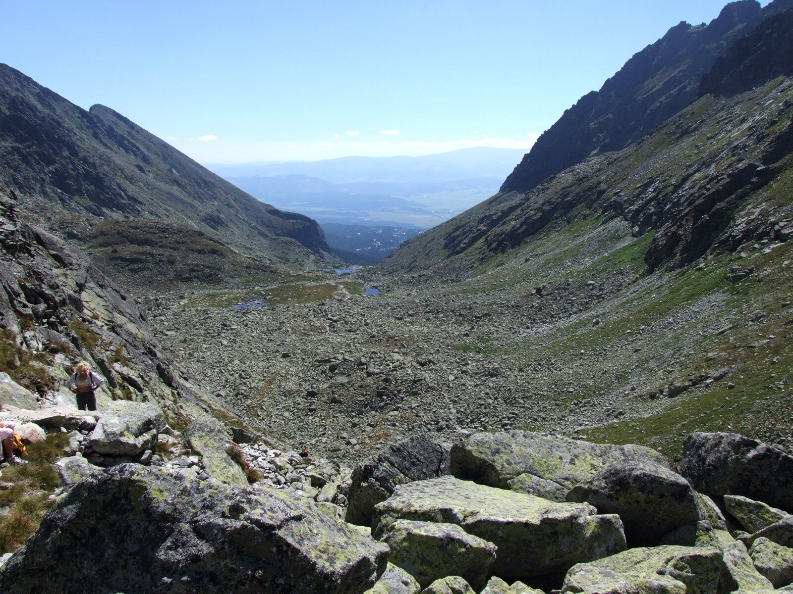 Centralną część fotografii zajmuje cyrk lodowcowy. Jest to zagłębienie w skale w kształcie zbliżonym do koła, wypełnione licznymi drobnymi odłamkami skalnymi, w niektórych częściach pokryte porostami. Po bokach znajdują się zbocza gór o dość stromym nachyleniu. W oddali, na drugim planie, rozległa dolina.