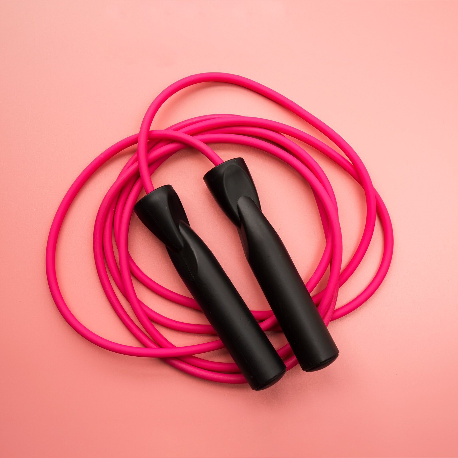 Ilustracja przedstawia różową skakankę z czarnymi rękojeściami, zwiniętą w kłębek. 