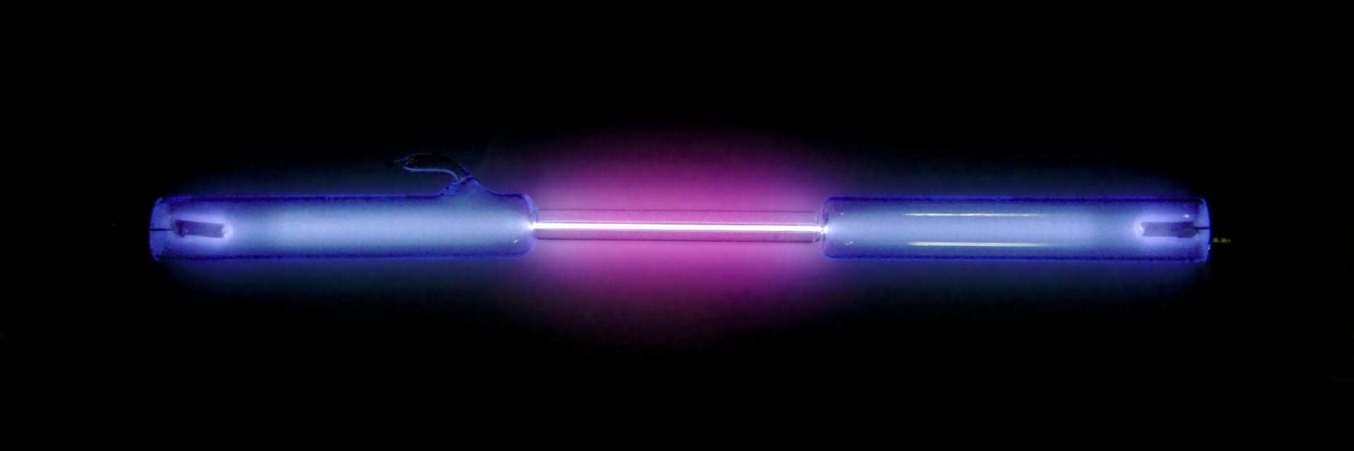 Zdjęcie przedstawia lampę wyładowczą w postaci szklanej rurki z dwiema elektrodami wypełnionej rozrzedzonym wodorem. Rurka ta w samym środku ma zwężony odcinek, który po podłączeniu elektrod do źródła prądu o wysokim napięciu świeci intensywnie purpurowym blaskiem.