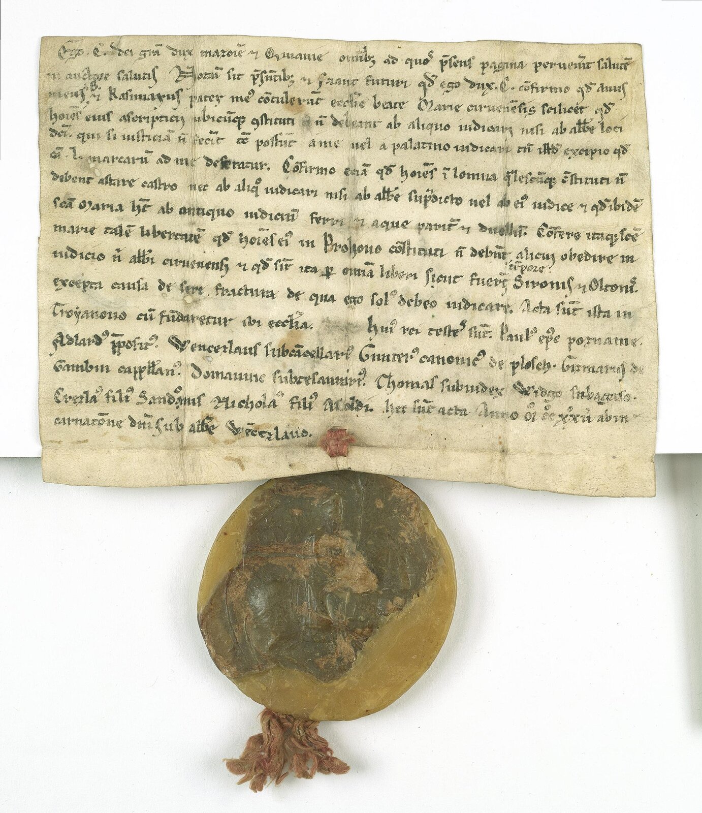 Zdjęcie przedstawia pożółkłą kartkę papieru, która została zapisana czarnym atramentem. Napisy nie są czytelne. U dołu papieru przypięta została okrągła żółto‑brązowa pieczęć. Przedmiot leży na białym tle.