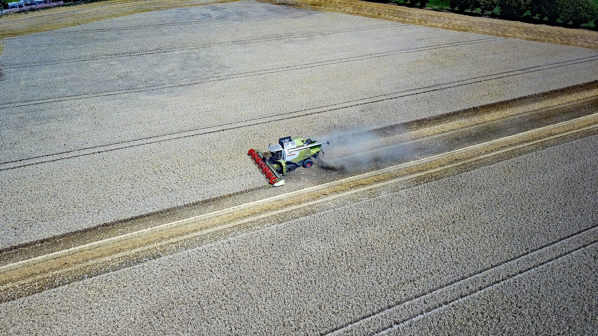 Zdjęcie lotnicze przedstawiające widok na kombajn zbożowy na rozległym polu.
