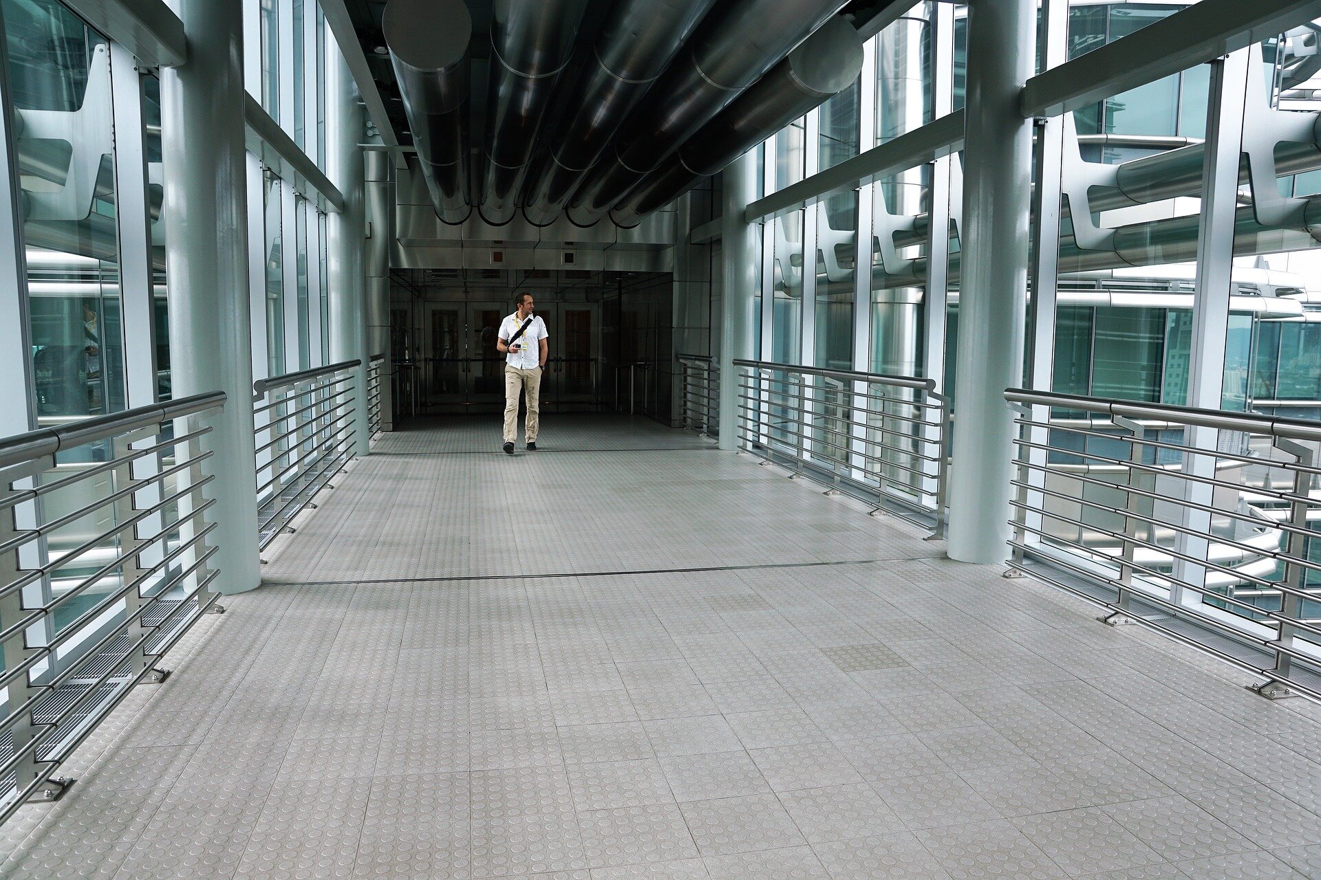 Zdjęcie przedstawia mężczyznę idącego korytarzem nowoczesnego budynku ze szkła i stali.