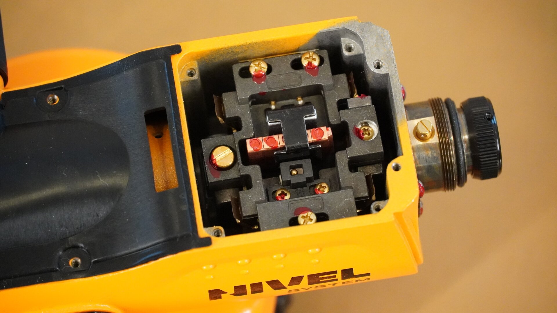 Zdjęcie przedstawia widok niwelatora z góry, po zdjęciu górnej osłony. Tuż za okularem widoczny jest kompensator ze śrubami w górnej części.