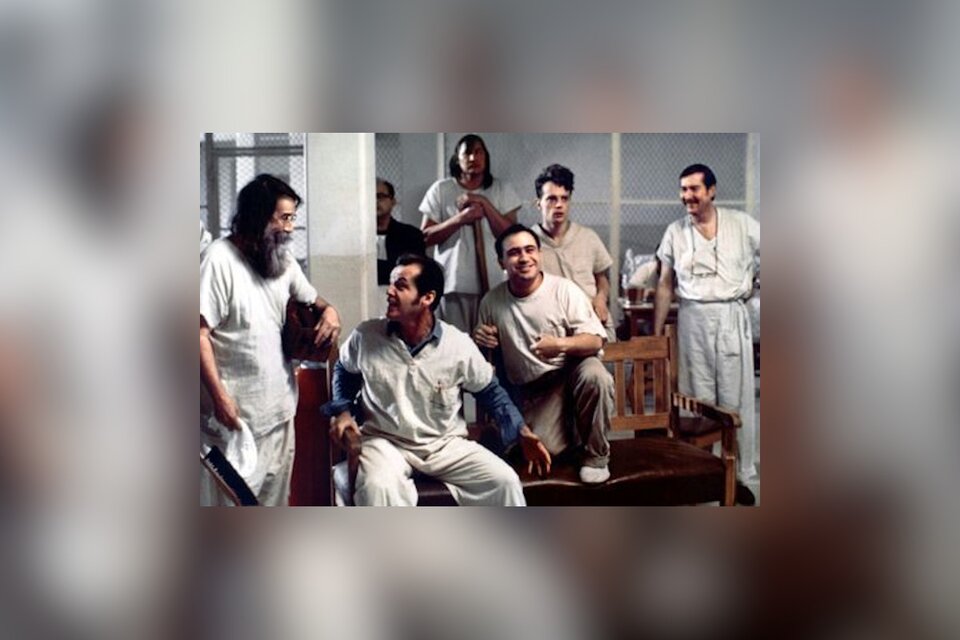 Zdjęcie przedstawia kadr z filmu Lot nad kukułczym gniazdem. Widać salę szpitalną, w której znajduje się grupa siedmiu mężczyzn w pidżamach. Mężczyźni rozmawiają ze sobą, niektórzy się śmieją.