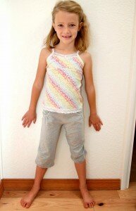 Ilustracja przedstawiająca dziewczynkę prosto stojącą przy ścianie z odsuniętymi od ciała rękami i dłońmi przylegającymi do ściany oraz rozstawionymi nogami.