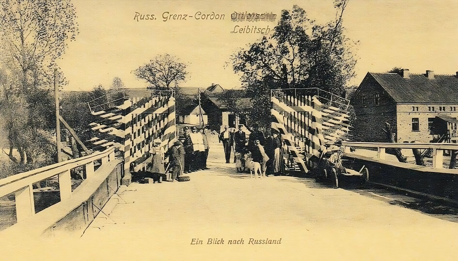 Zdjęcie przedstawia posterunek graniczny ulokowany na moście. Przy przejściu stoi kilka osób: mężczyźni w mundurach, kobieta w długiej sukni oraz dzieci. Po prawej stronie oraz w oddali widać domy i drzewa.