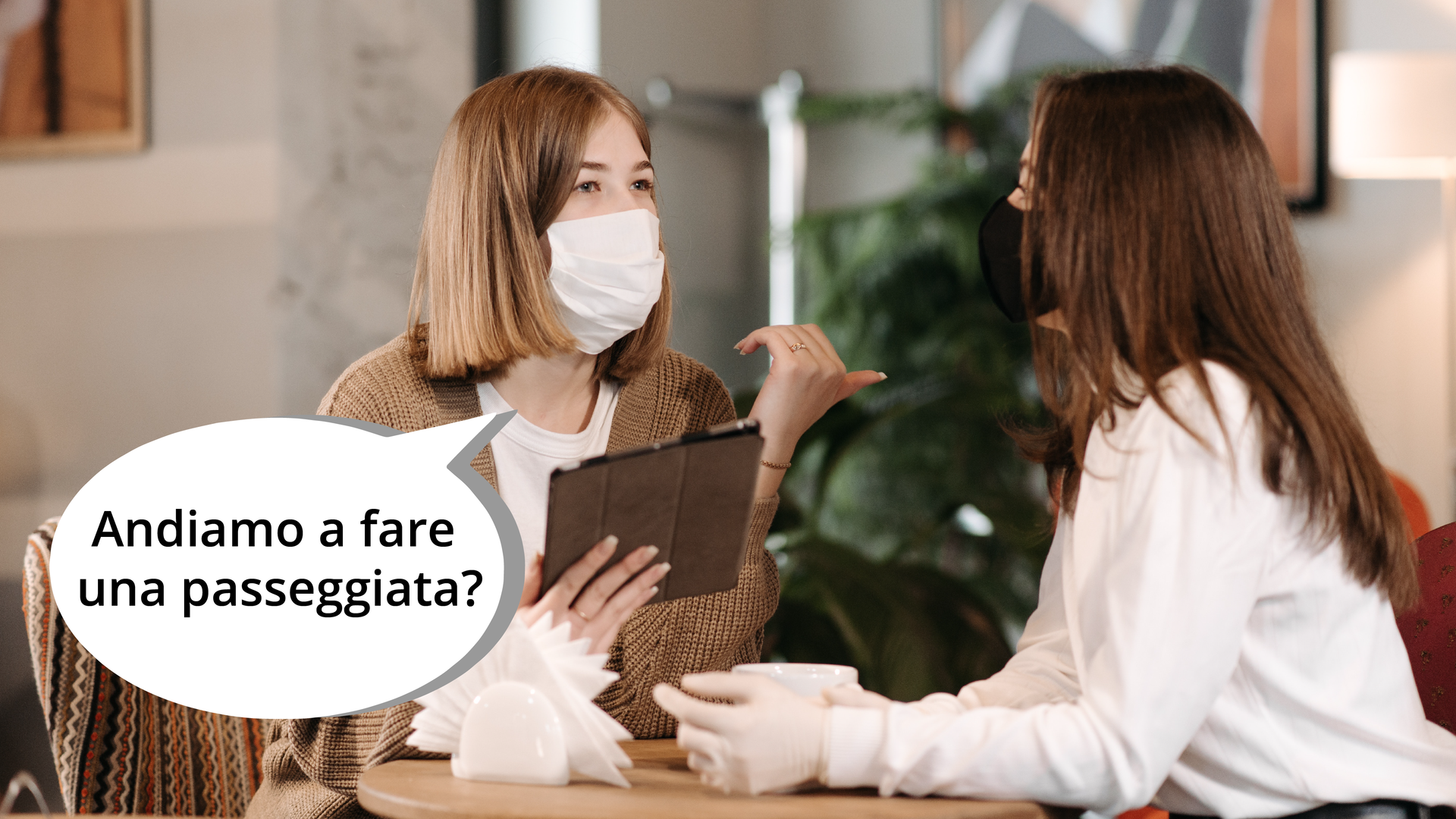 Zdjęcie przedstawia dwie kobiety siedzące przy stoliku i rozmawiające ze sobą. Obok kobiety wskazującej kciukiem wyjście znajduje się dymek z pytaniem: Andiamo a fare una passeggiata?