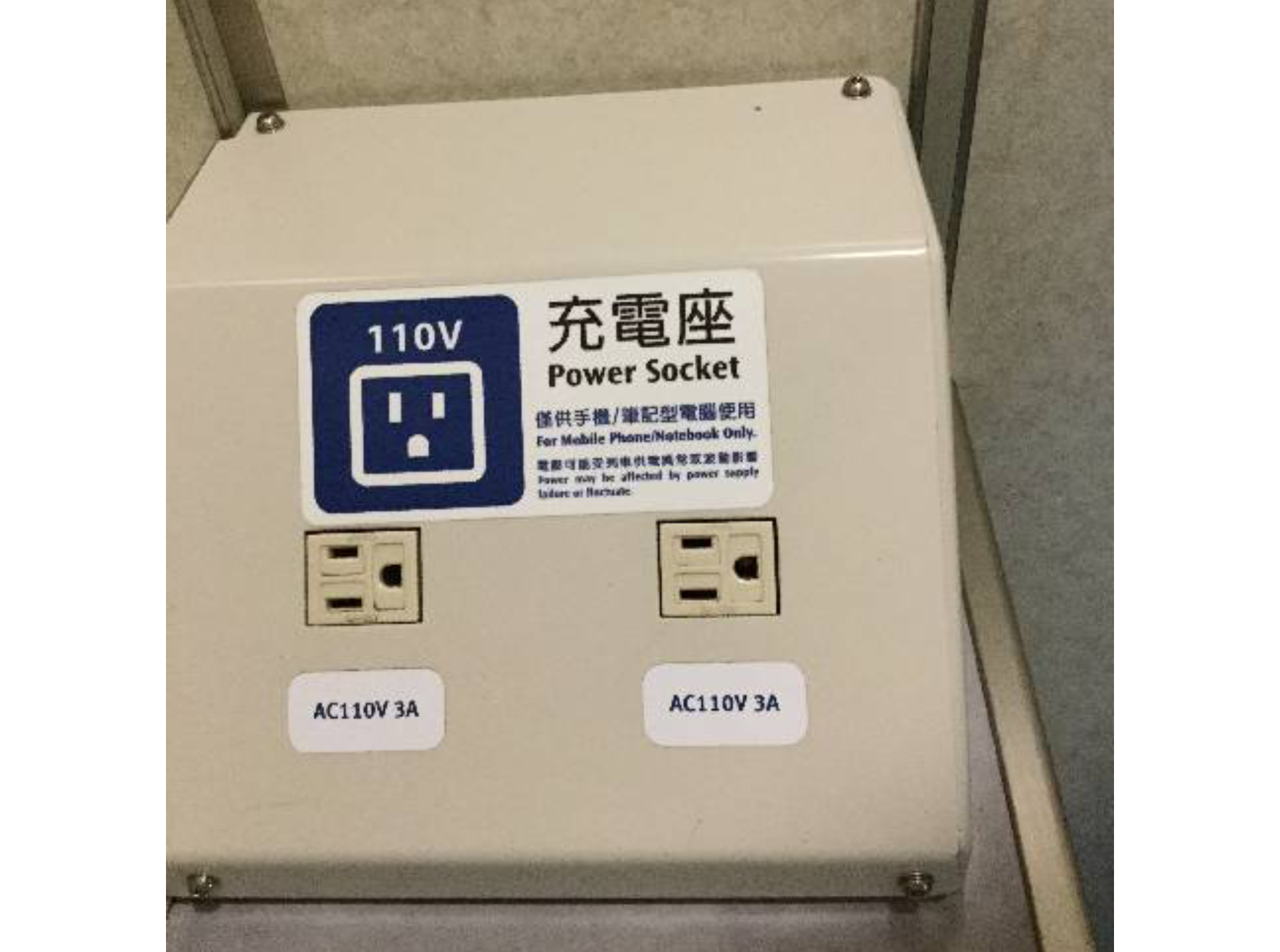 Zdjęcie. Metalowa skrzynka z dwoma gniazdkami o napięciu stu dziesięciu woltów. Są to gniazdka na wtyczki z bolcami prostopadłościennymi, a nie jak w Polsce, okrągłymi. Pod każdym z gniazdek podpis: AC110 V 3 A. Nad gniazdkami naklejka z informacją o napięciu w gniazdkach.