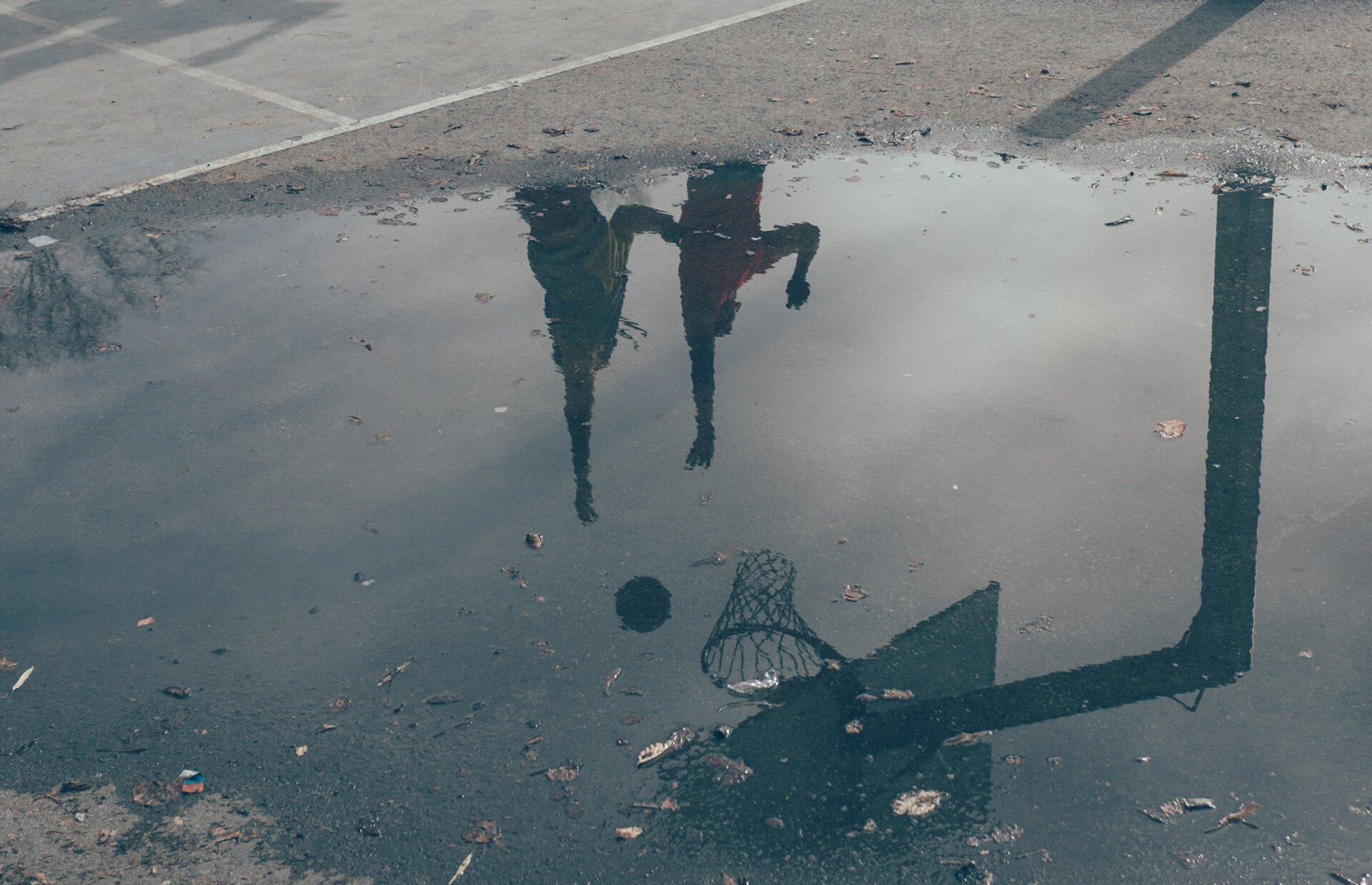Fotografia przedstawia kałużę, w której odbijają się dwie osoby grające w koszykówkę.