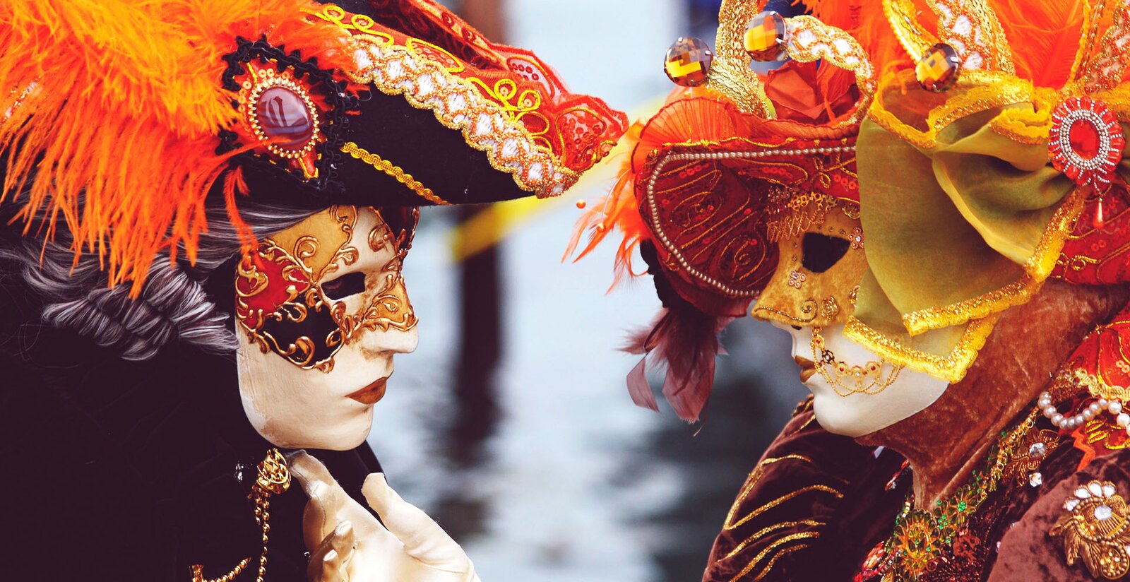 Zdjęcie przedstawia ujęte z profilu głowy dwóch osób ustawionych naprzeciw siebie jak w odbiciu lustrzanym. Ubrane są one najprawdopodobniej w stroje karnawałowe. Obie mają całe twarze skryte za maskami, które przedstawiają twarze ludzkie również w maskach, z tym że te zasłaniają tylko górną część „twarzy maski” tak, że widoczna jest część od nosa w dół z ustami pokrytymi czerwoną farbą. Maska osoby z lewej strony ma rysy mężczyzny, natomiast z prawej, kobiety. Obie osoby mają też bogato zdobione kapelusze z piórami i kokardami przypiętymi broszami. Kapelusz tej z lewej jest czarny, podobnie jak widoczny fragment, spiętego pod szyją złotą broszą z łańcuszkiem, płaszcza. Kolor kapelusza osoby po prawej jest czerwony i w takim kolorze jest również ukazany na fotografii fragment bogato zdobionej sukni. Widać również dłoń w białej rękawiczce, którą osoba nosząca maskę kobiecą dotyka brody maski męskiej.