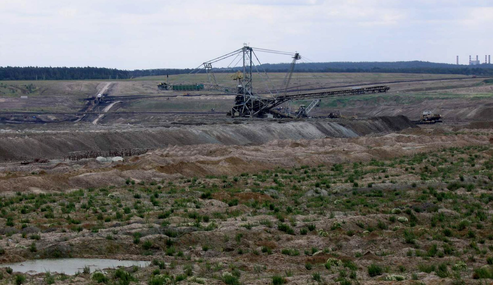 Na zdjęciu rozległe wykopy, maszyny i urządzenia. W tle kominy.