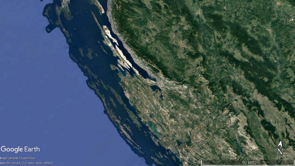 Zdjęcie satelitarne przedstawia wybrzeże dalmatyńskie. Ląd zaznaczony jest kolorem zielonym, a woda niebieskim. Charakteryzuje się licznymi cieśninami pomiędzy wydłużonymi pasmami górskimi a brzegiem.