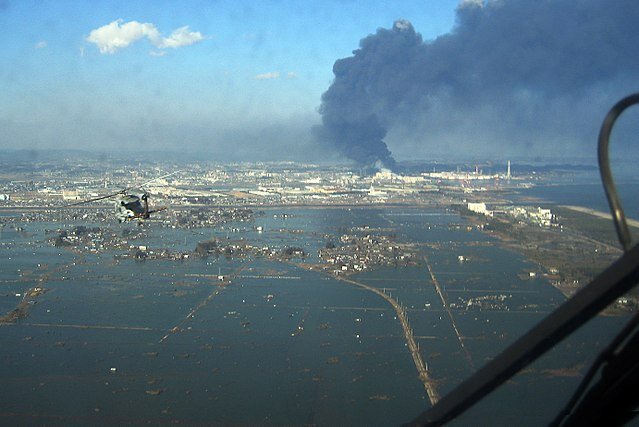 Zdjęcie z helikoptera przedstawia trzęsienie ziemi i tsunami w Sendai w Japonii. Niemal całkowicie zalane wodą miasto. W oddali dym pożaru i budynki, które nie znalazły się pod wodą.    