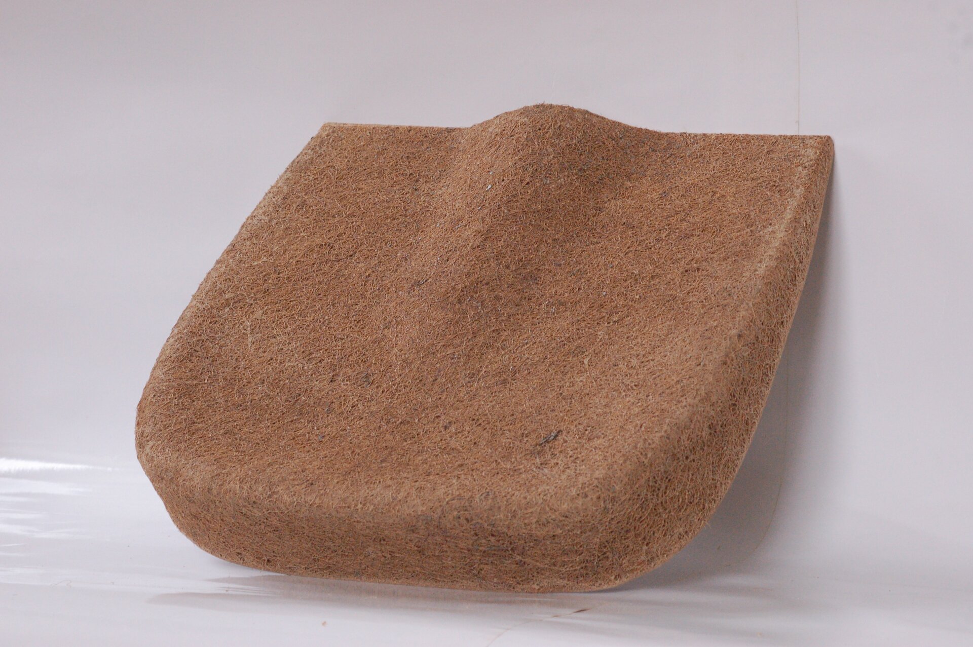 Zdjęcie przedstawia siedzisko z włókna kokosowego. W dolnej części i pośrodku na górze siedzisko jest wypukłe.