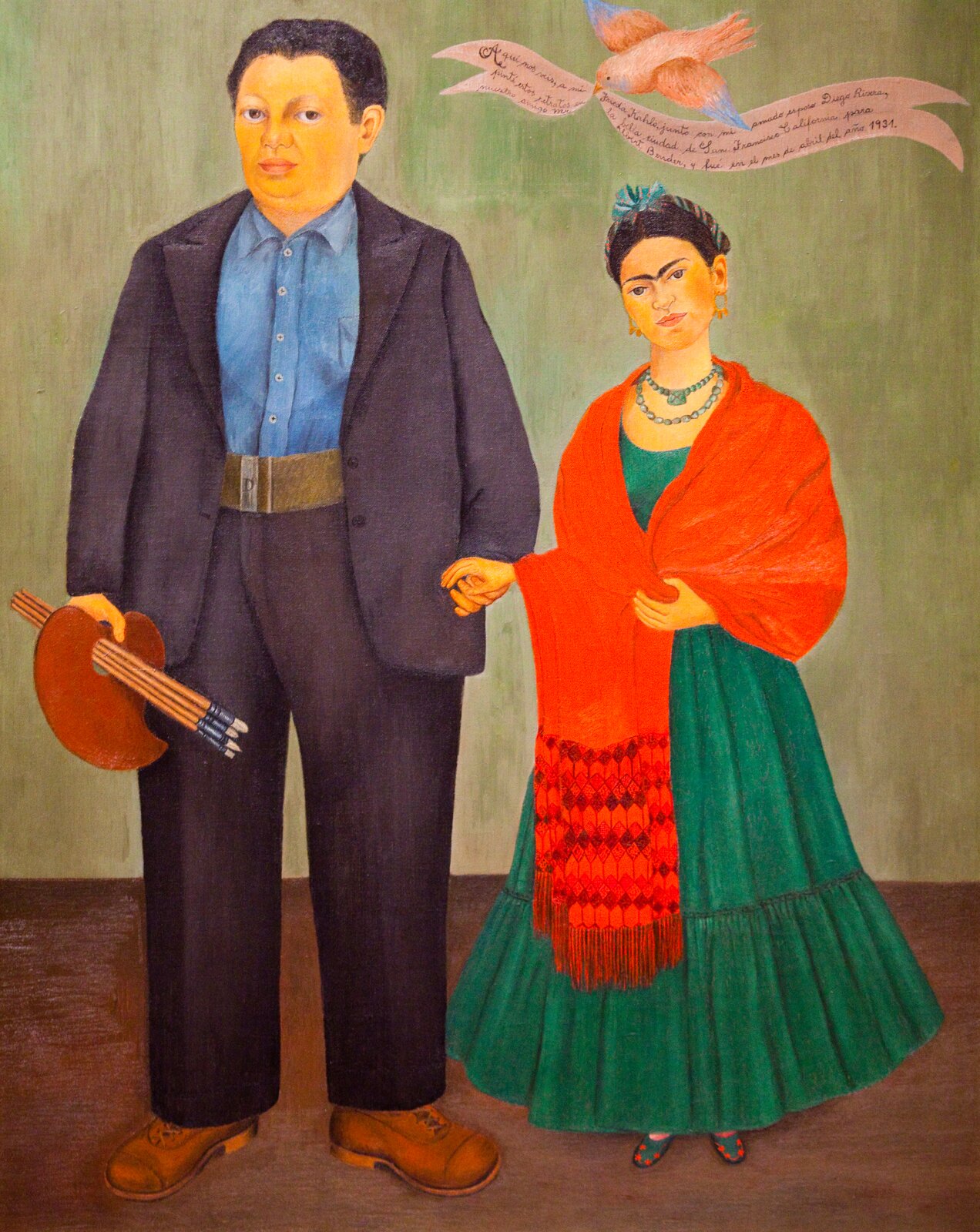 Ilustracja przestawia obraz Fridy Kahlo „Frida i Diego Rivera”. Na obrazie widać dwie stojące osoby - mężczyznę i kobietę trzymających się za rękę. Mężczyzna jest bardzo postawny ubrany w grafitowy garnitur i niebieską koszulę. W prawej ręce trzyma paletę i pędzle. Kobieta jest ubrana w zieloną sukienkę, a na ramionach ma pomarańczową chustę. Na szyi ma korale, a we włosach wczepioną kokardę. Na głową kobiety unosi się ptak, trzymający w dziobie wstążkę, na której jest tekst. Pozują w pokoju z jasną ścianą i ciemnobrązową podłogą.