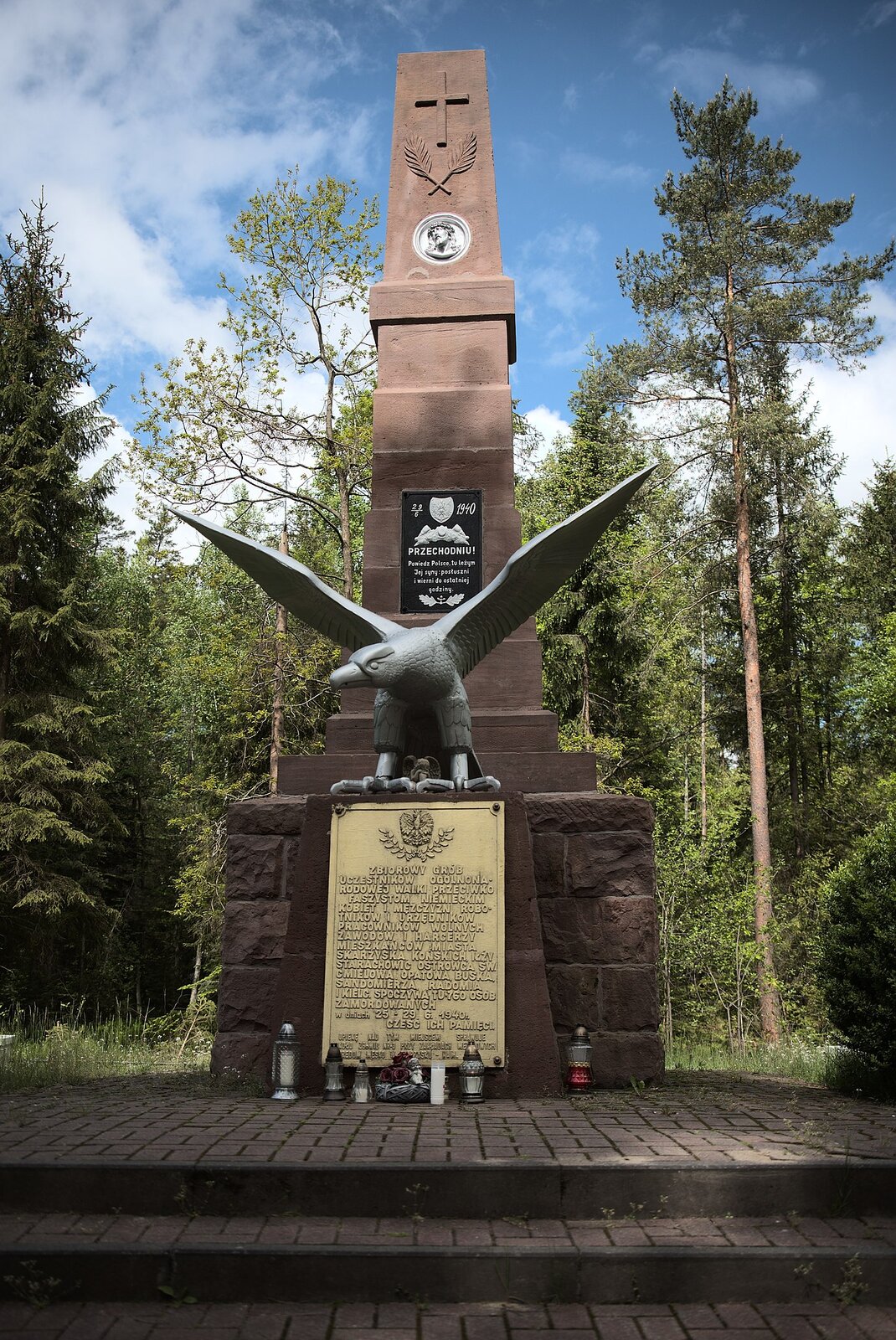 Zdjęcie przedstawia pomnik stojący pośród drzew. To wysoki obelisk, na podstawie którego znajduje się orzeł z rozpostartymi skrzydłami. Pod nim znajduje się tablica z napisem: Zbiorowy grób uczestników ogólnonarodowej walki przeciwko faszystom niemieckim: kobiet i mężczyzn, robotników i urzędników, pracowników wolnych zawodów i harcerzy, mieszkańców miasta Skarżyska, Końskich, Iłży, Starachowic, Ostrowca Świętokrzyskiego, Chmielowa, Opatowa, Buska, Sandomierza, Radomia i Kielc. Spoczywa tu 760 osób zamordowanych w dniach 25‑29 czerwca 1940. Cześć ich pamięci. Nad orłem, na obelisku kolejna tablica z napisem: 29.6.1940 Przechodniu! Powiedz Polsce, tu leżym Jej syny: posłuszni i wierni do ostatniej godziny. Na górze obelisku znajduje się twarz Jezusa Chrystusa w koronie cierniowej, a nad nią dwa palmowe liście i krzyż.