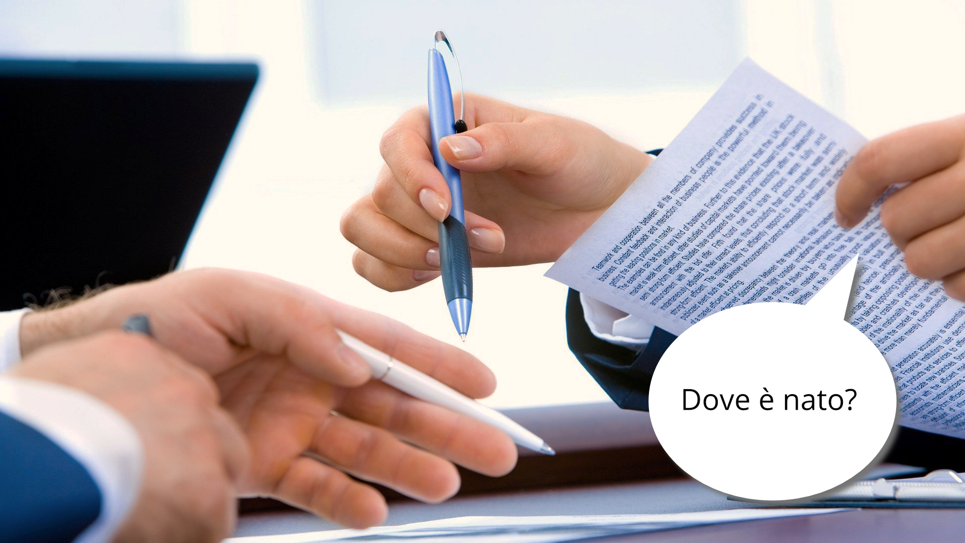 Zdjęcie przedstawia zbliżenie na ręce dwóch osób, które trzymają długopisy w ręku i wypełniają jakiś formularz. Po prawej stronie znajduje się dymek z tekstem: "Dove è nato?"