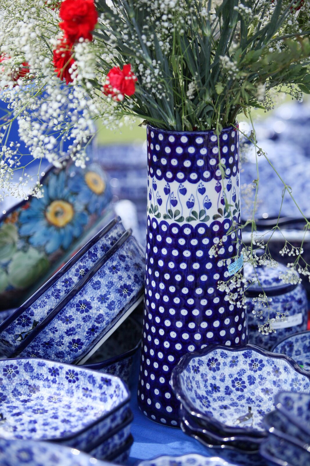 Ilustracja przedstawia zestaw ceramiki, którego centralnym elementem jest wazon. Jest to ceramika w niebiesko-białym kolorze wyglądająca na ręcznie zdobioną. Jest to ceramika bolesławiecka, produkt wykonany z kamionki.