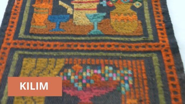 Zdjęcie fragmentu ciemnego kilimu o jaskrawym wzorze, który przedstawia naczynia kuchenne. 