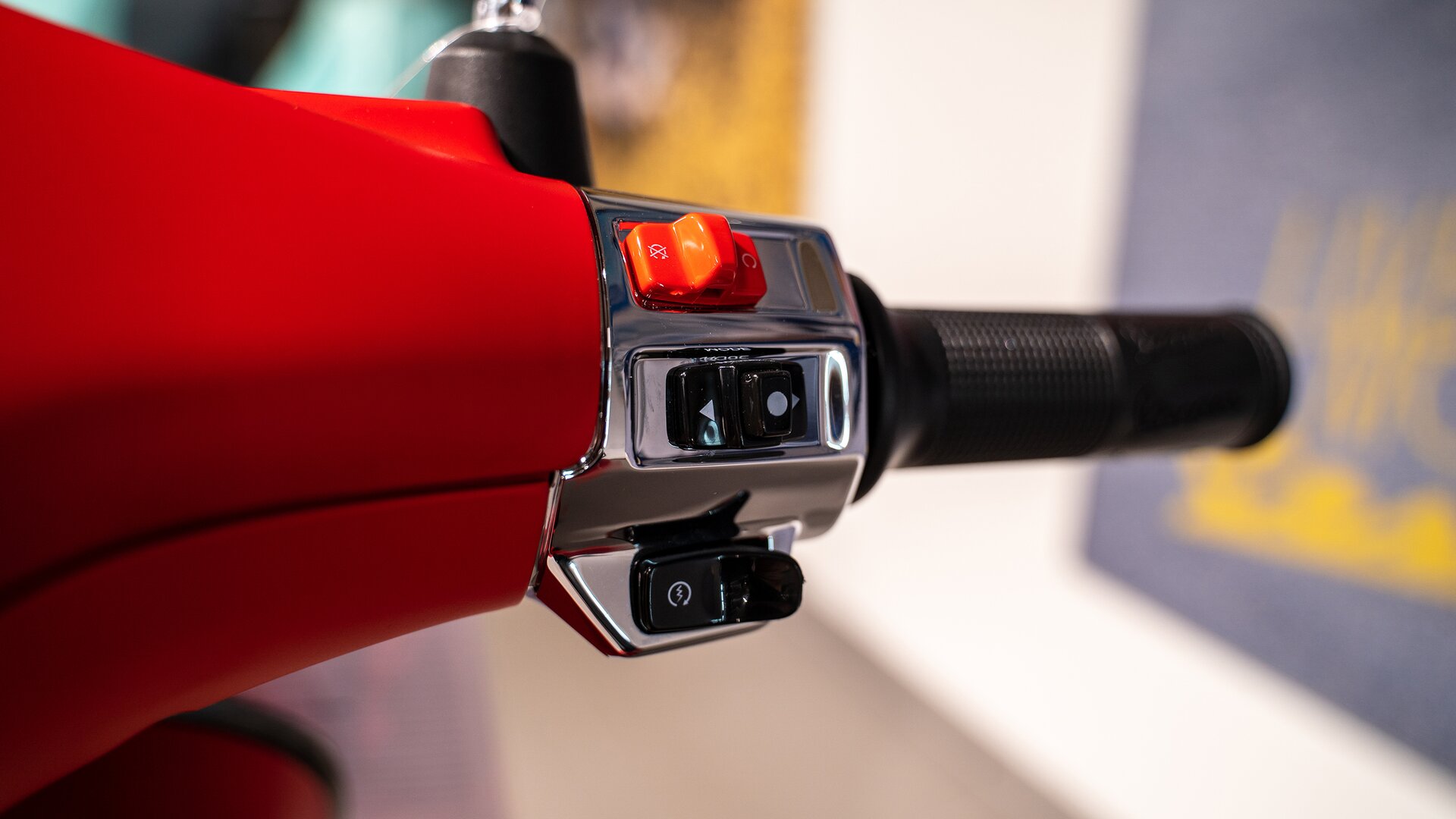 Zdjęcie przedstawia zbliżenie na kierownicę skutera. Są tam czarne i jest czerwony przełącznik. 