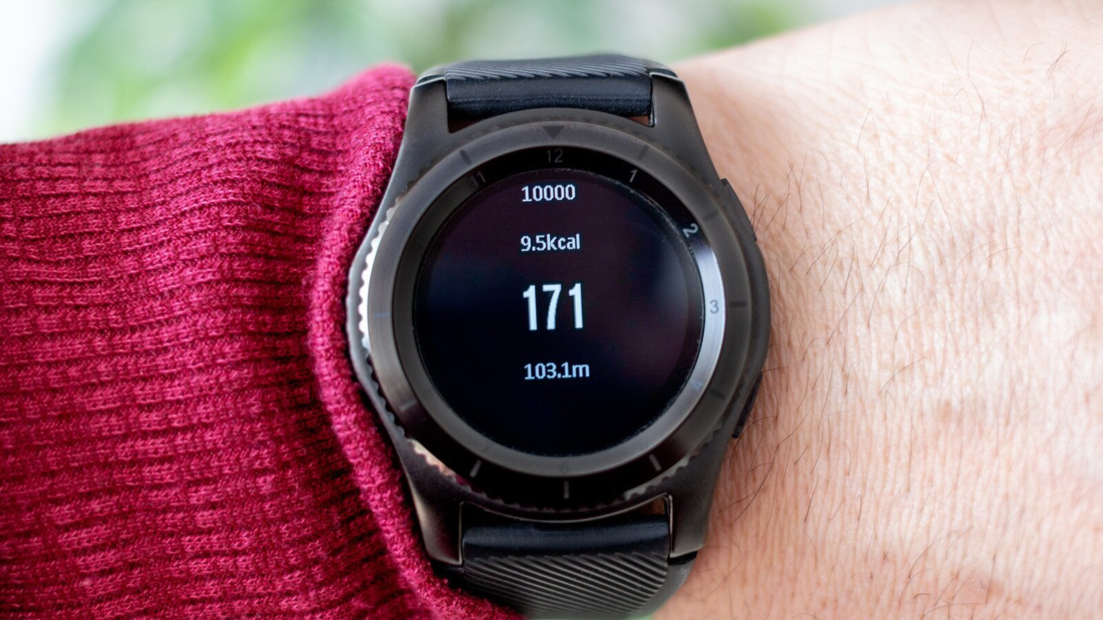  Poprawiony opis:  Zdjęcie przedstawia nadgarstek, na którym znajduje się zegarek typu smartwatch. Na czarnej tarczy zegarka widoczne są dane, takie jak: 10000 (liczba kroków), 9.5 kcal (spalone kalorie), 171 (tętno) oraz 103.1 m (pokonany dystans). Zegarek posiada metalową kopertę i czarny pasek.