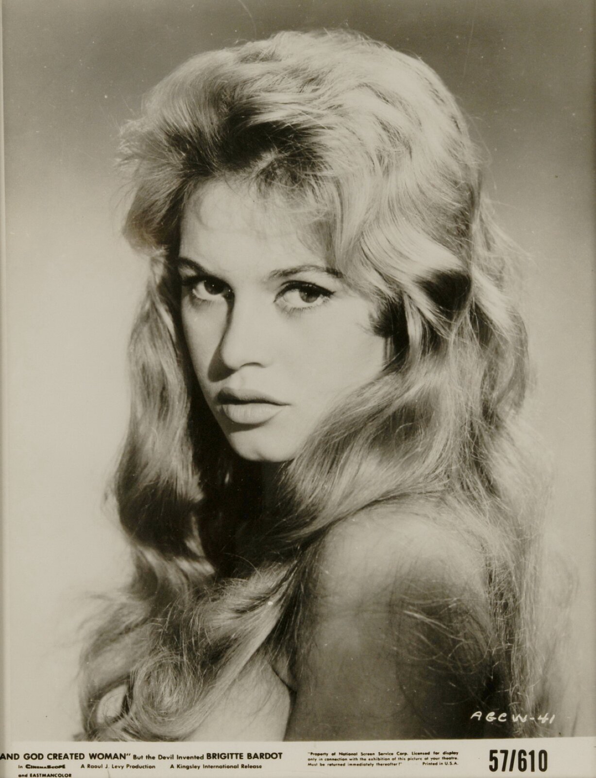 Fotografia przedstawia plakat promujący film „I Bóg stworzył kobietę”. Na pierwszym planie obecna jest Brigitte Bardot - młoda, blondwłosa kobieta, spoglądająca w stronę obiektywu. Na jej oczach można zauważyć makijaż w postaci ciemnej kreski na górnej linii rzęs, jej skóra jest jasna, a usta lekko rozchylone. Kobieta ma krótką grzywkę, częściowo zaczesaną do tyłu, a średniej długości włosy przykrywają jej nagą skórę.  Pod wizerunkiem aktorki widoczny jest biały pasek, na którym zostały zawarte informacje o filmie.