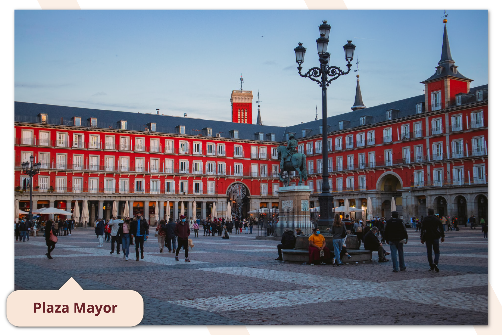 Zdjęcie przestawia plac znajdujący się w centrum Madrytu. Wokół placu rozciąga się czerwona kamienica. Na placu chodzą ludzie. Podpis na zdjęciu Plaza Mayor.
