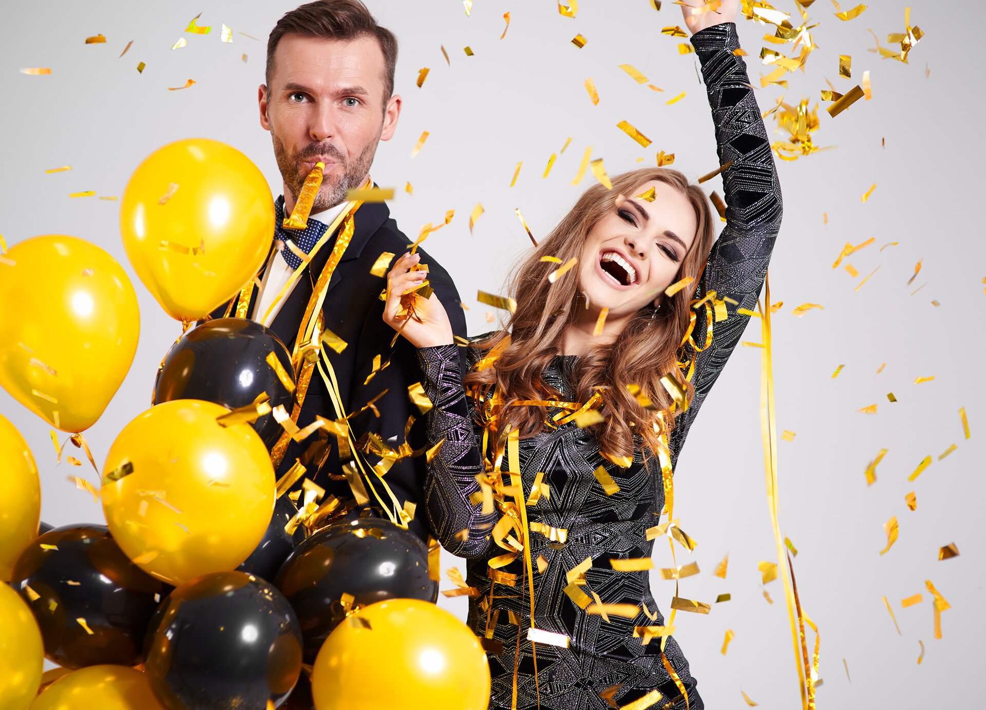 Zdjęcie przedstawia kobietę i mężczyznę w odświętnych strojach, na których spada konfetti. Mężczyzna trzyma żółte i czarne balony. 