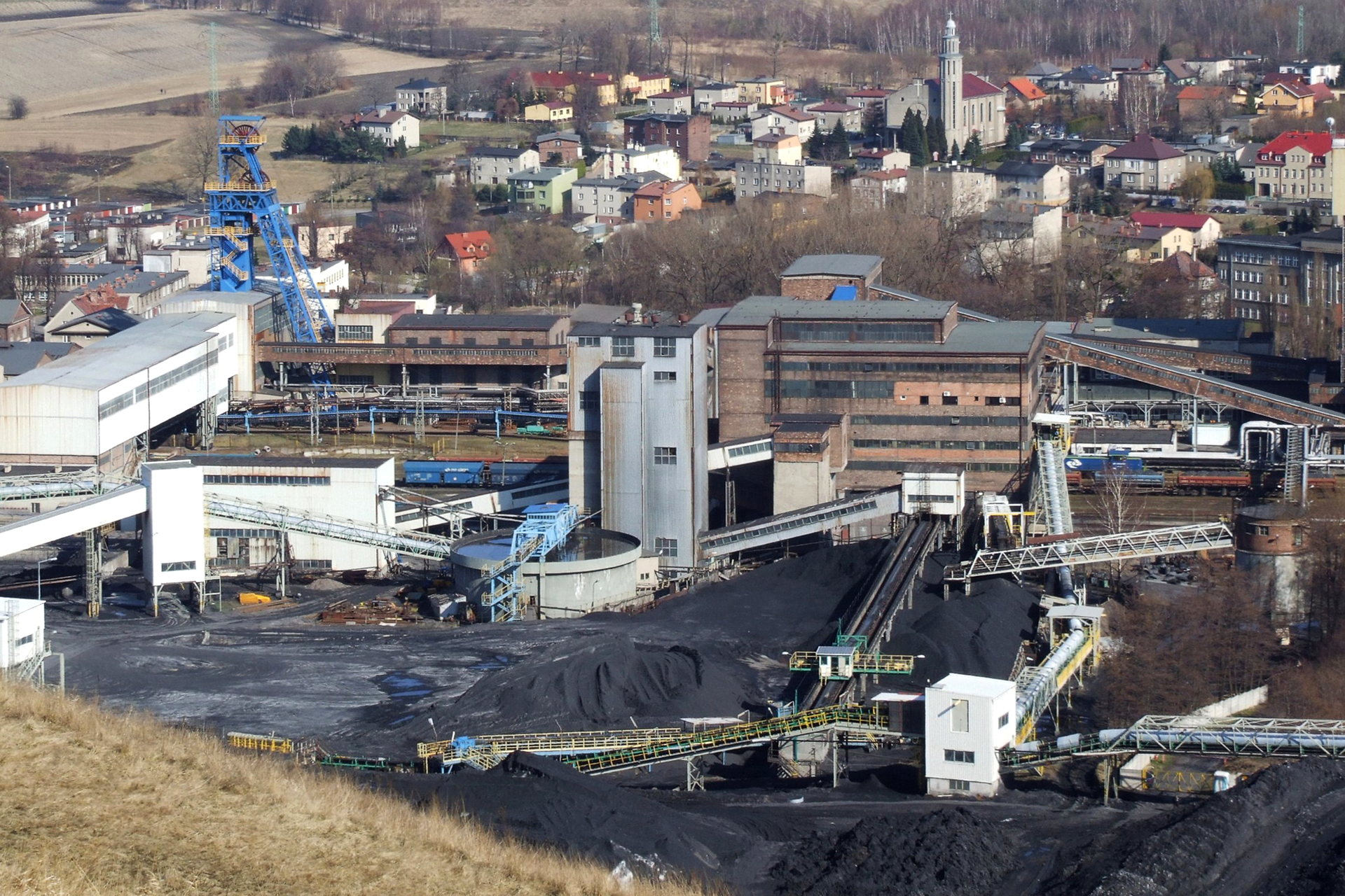 Fotografia prezentująca teren kopalni węgla kamiennego. Widoczne liczne zabudowania oraz hałdy węgła.