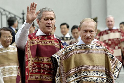 Na zdjęciu znajdują się dwaj dojrzali mężczyźni. Są to od lewej George W. Bush  oraz Władimir Putin. Mężczyzna po lewej stronie macha ręką. Mężczyźni mają założone charakterystyczne folklorystyczne kamizelki. 
