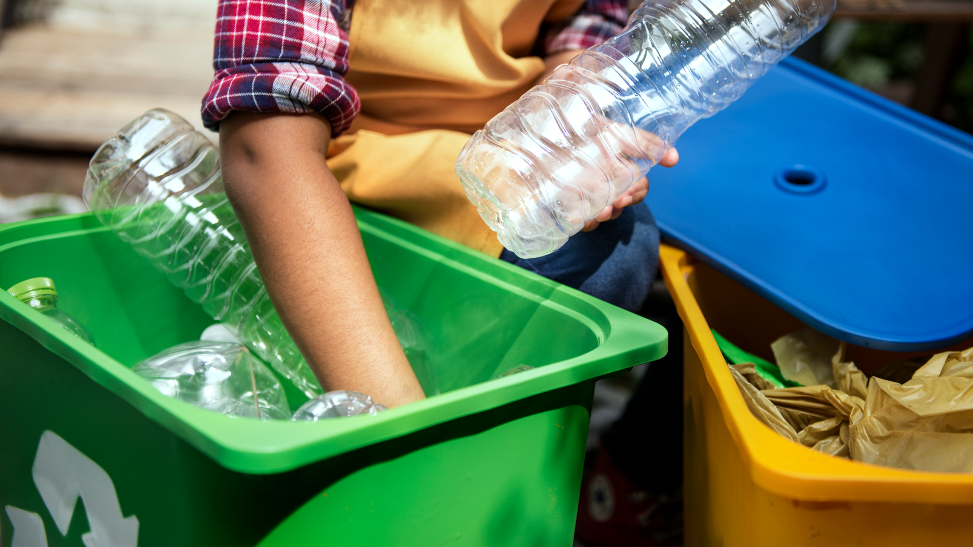Zdjęcie przedstawia ręce osoby, która wkłada do pojemnika na śmieci butelki plastikowe.