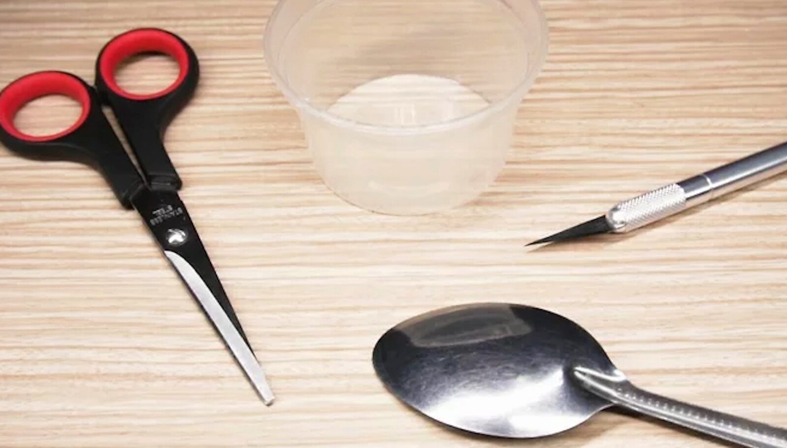 Zdjęcie przedstawia nożyczki, pustą plastikową miseczkę, nożyk i metalową łyżkę.