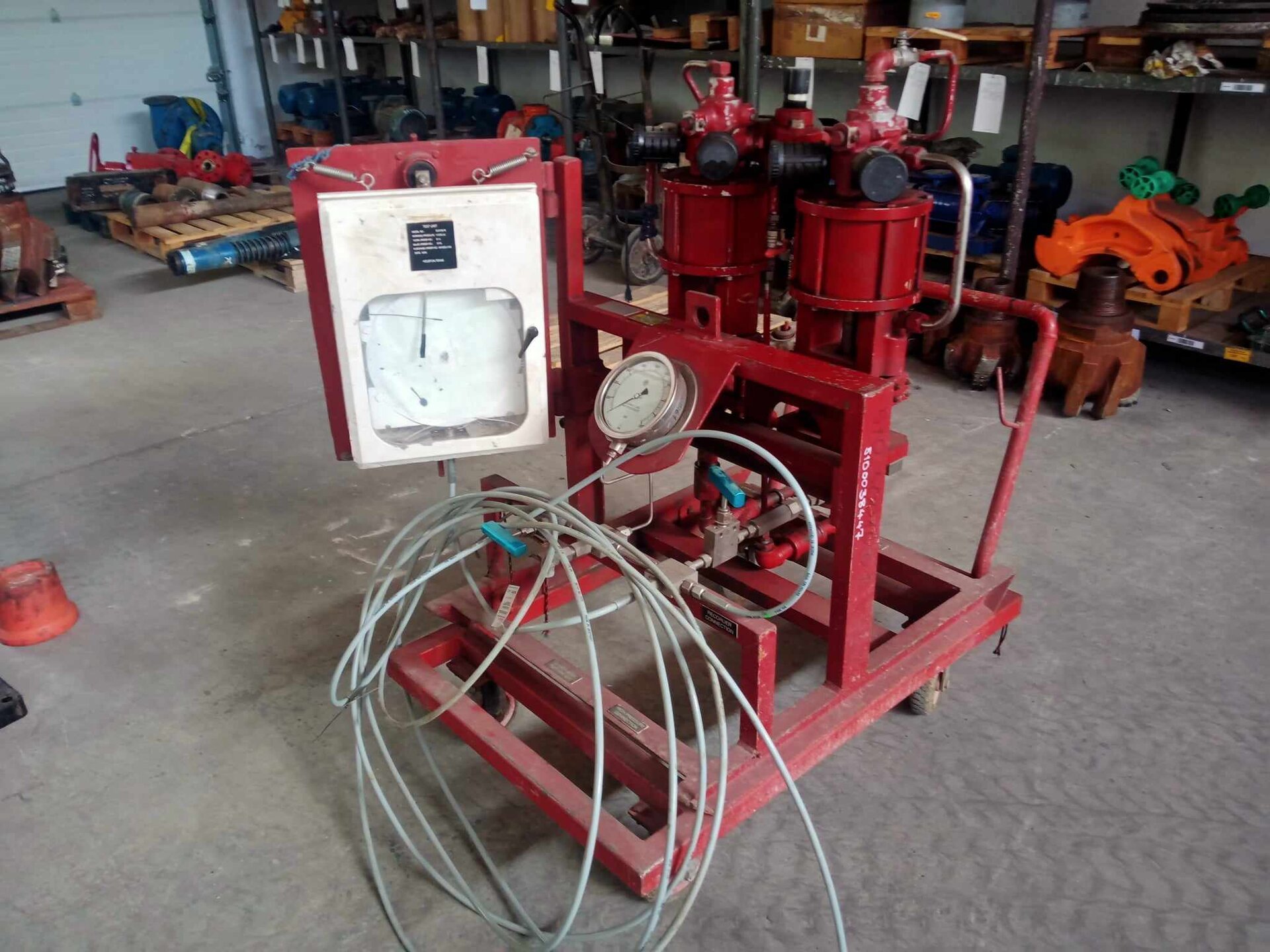 Na zdjęciu widoczne jest urządzenie do wykonywania testów szczelności, jednostka testowa. Składa się ona z metalowego stelaża na kółkach. W przedniej części znajduje się duża tarcza manometru wraz z długim cienkim przewodem podłączonym za pomocą zaworu do tylnej części urządzenia. W tylnej części urządzenia znajdują się dwa zbiorniki. Na lewo od tarczy manometry znajduje się rekordograf.