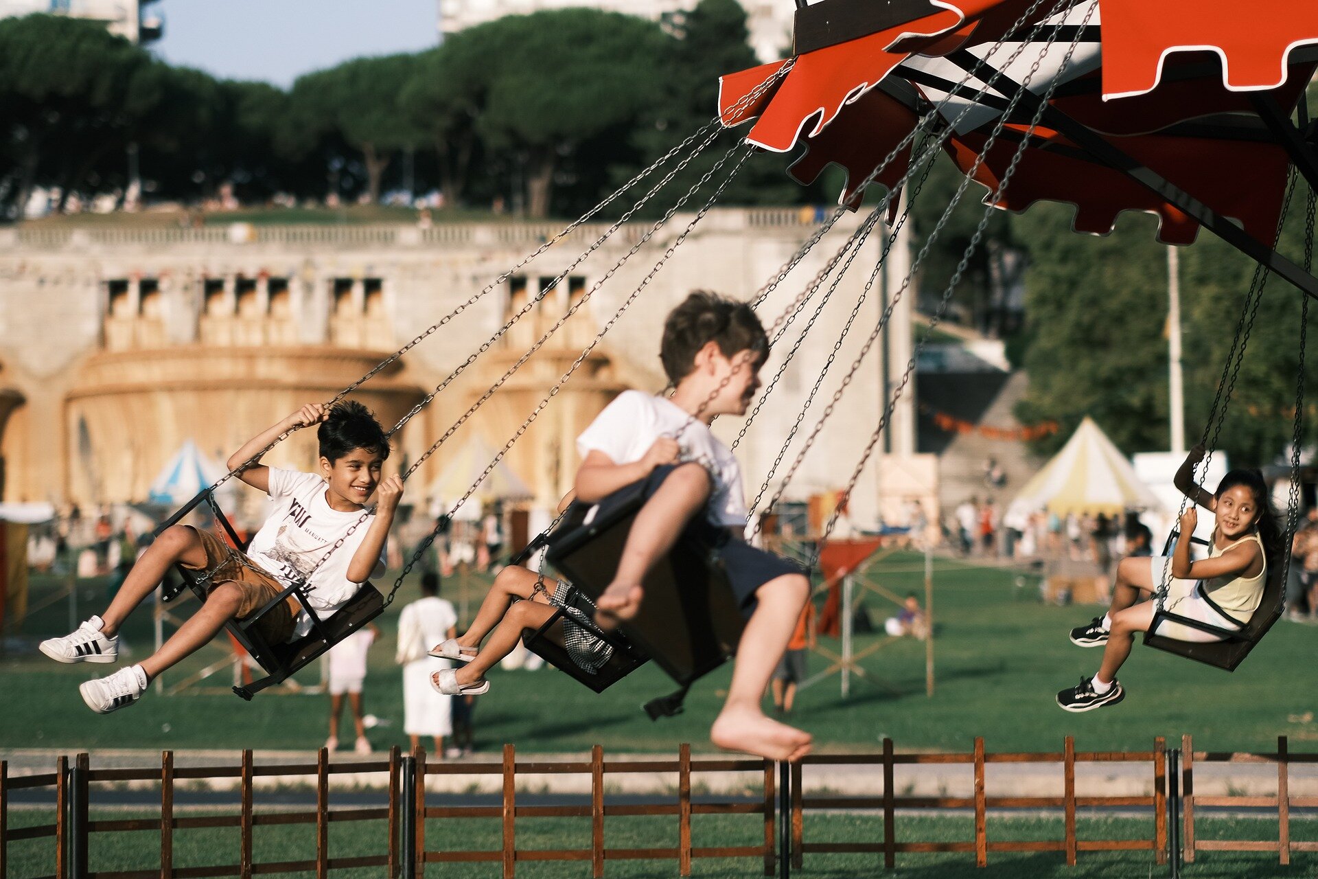 Ilustracja ukazuje park rozrywki, gdzie w pierwszym planie znajduje się karuzela. Na krzesłach, zawieszonych na długich łańcuchach, siedzą dwaj chłopcy i jedna dziewczynka, unoszą się w powietrzu uśmiechnięci. Zadanie alternatywne wyświetla się w trybie dostępności.