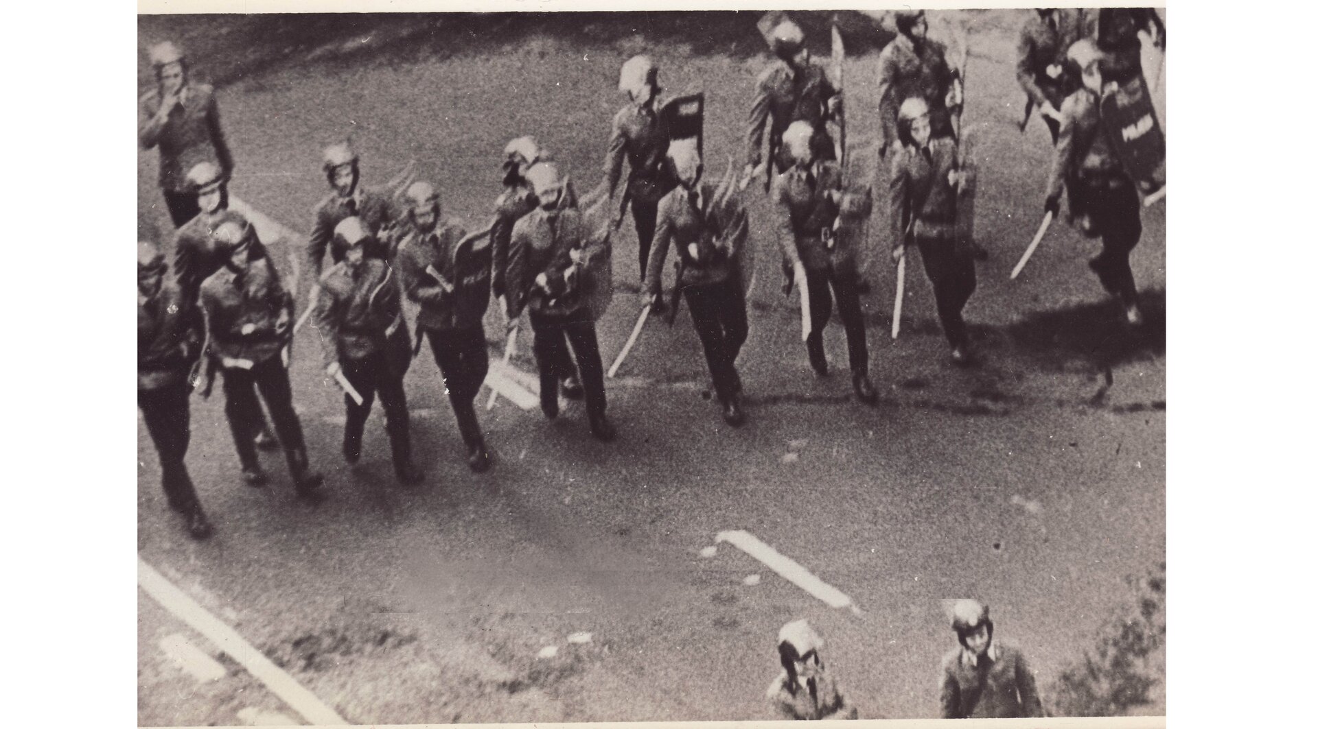 Czarno-biała fotografia przedstawiająca funkcjonariuszy ZOMO z wyposażeniem bojowym w czasie akcji przeciw demonstrantom (1981 r.).