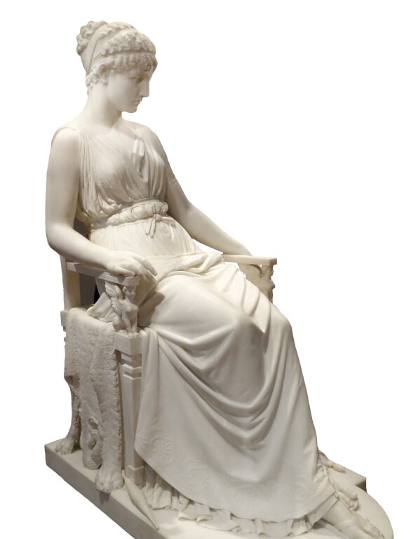 Biała rzeźba kobiety. Postać siedzi na krześle, ma zamyślony wyraz twarzy. White sculpture of a woman. The figure sits on a chair, has a thoughtful look on his face.