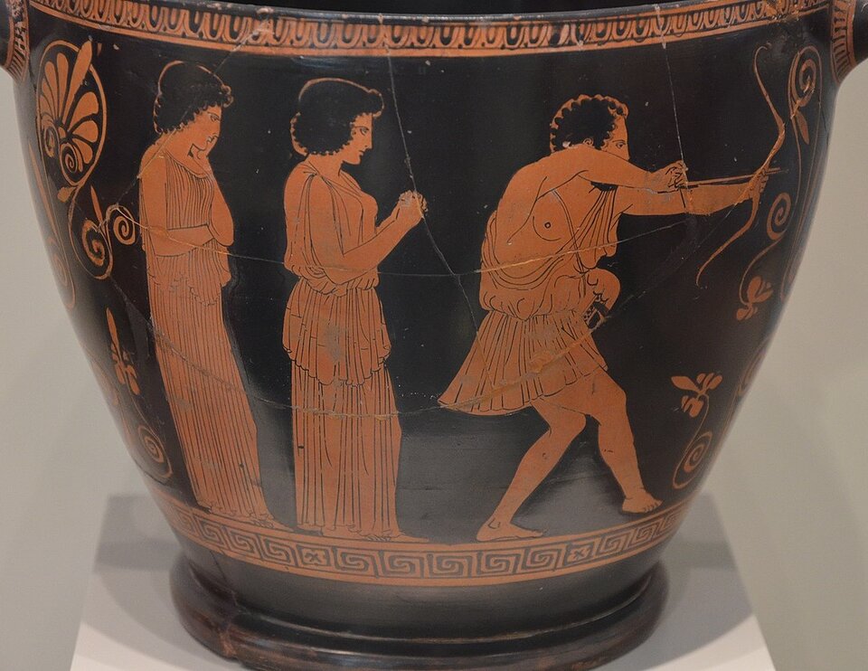 Zdjęcie przedstawia starożytną wazę czerwonofigurową. Rysunek na wazie przedstawia dwie kobiety i strzelającego z łuku mężczyznę. Od lewej strony stoją dwie kobiety w peplosach. Jedna dotyka twarzy lewą ręką, a druga ma złączone ręce wyciągnięte przed siebie. Obydwie kobiety patrzą na stojącego przed nimi mężczyznę, który wygląda jakby się skradał. Naciągnął łuk i zaraz odda strzał. Mężczyzna nosi krótki chiton, ma odkrytą część torsu.