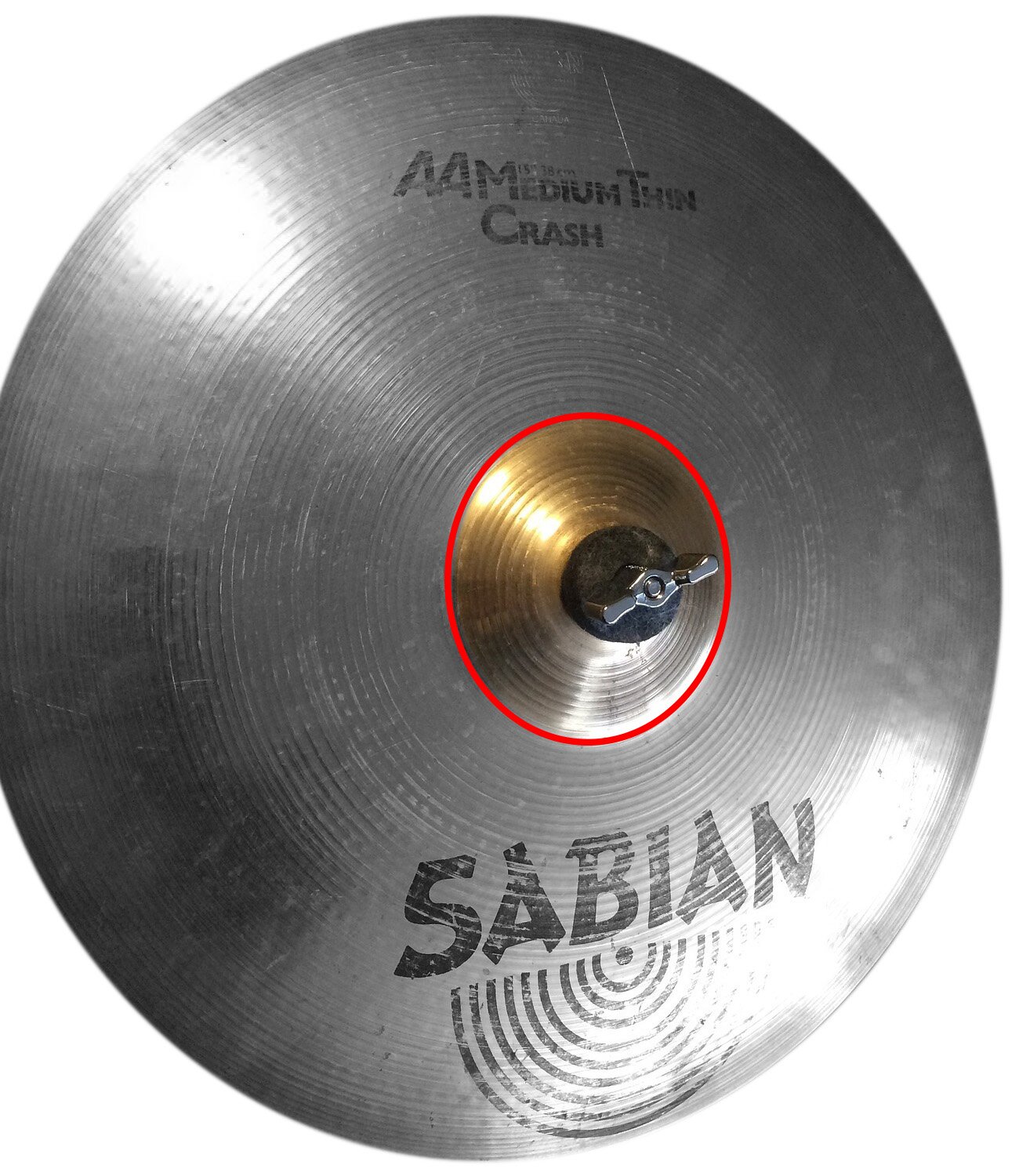 Zdjęcie przedstawia okrągły talerz perkusyjny w kolorze srebrny, z lekko wypukłą, okrągłą częścią pośrodku w kolorze złotym, otoczoną okręgiem w kolorze czerwonym, w której umieszczone jest czarne pokrętło motylkowe. W górnej i dolnej części talerza czarne napisy i logo.