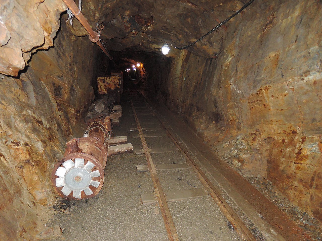 Zdjęcie jednego z korytarzy kopalni. Jest wąski i niski, pośrodku biegną wąskie tory. Wykuty w skale.