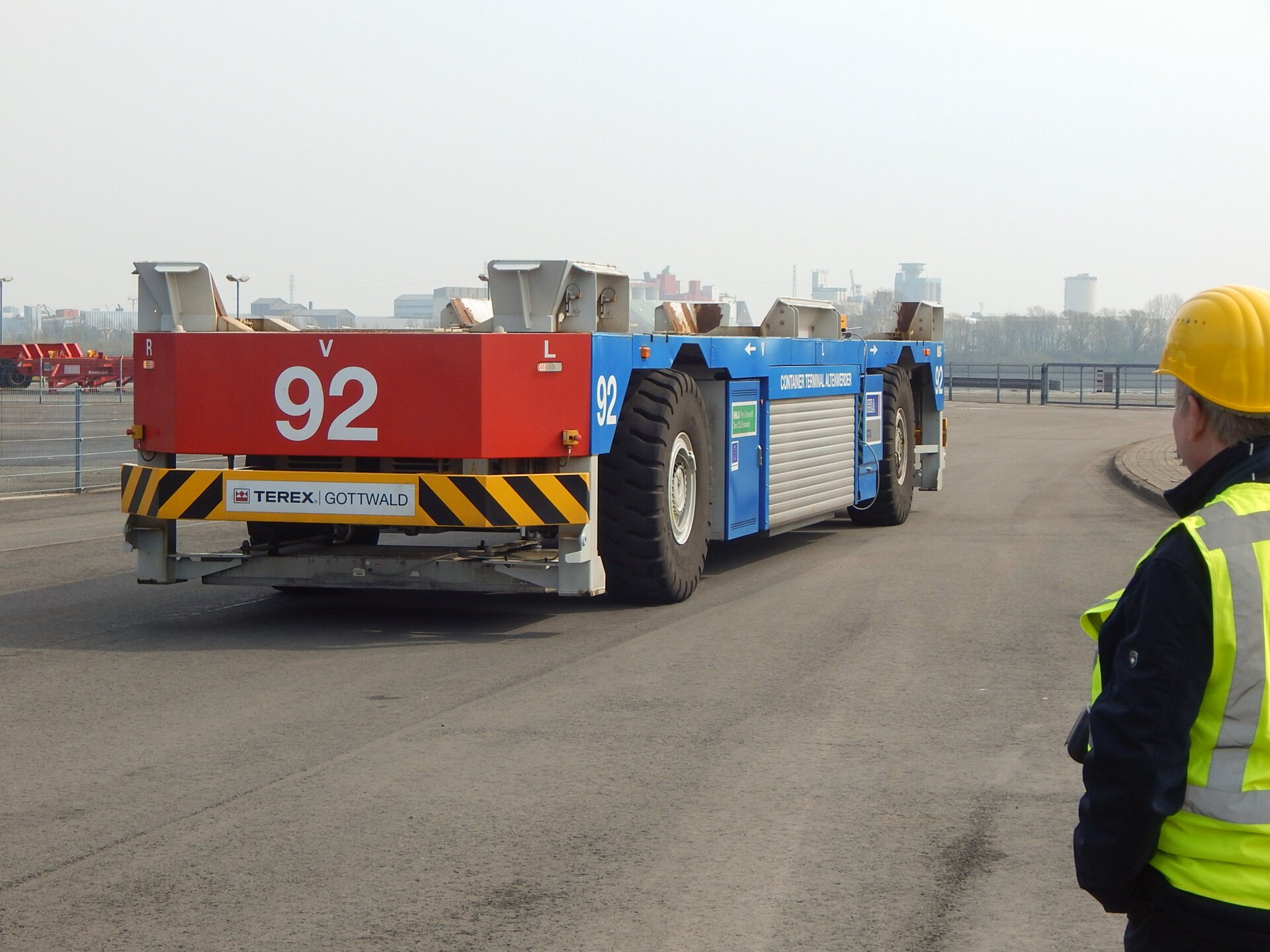 Na zdjęciu widoczny otwarty teren na nim wóz transportowy bezzałogowy do obsługi zdalnej. Na platformie widoczne uchwyty, które zabezpieczają, przewożone w kontenerach ładunki .